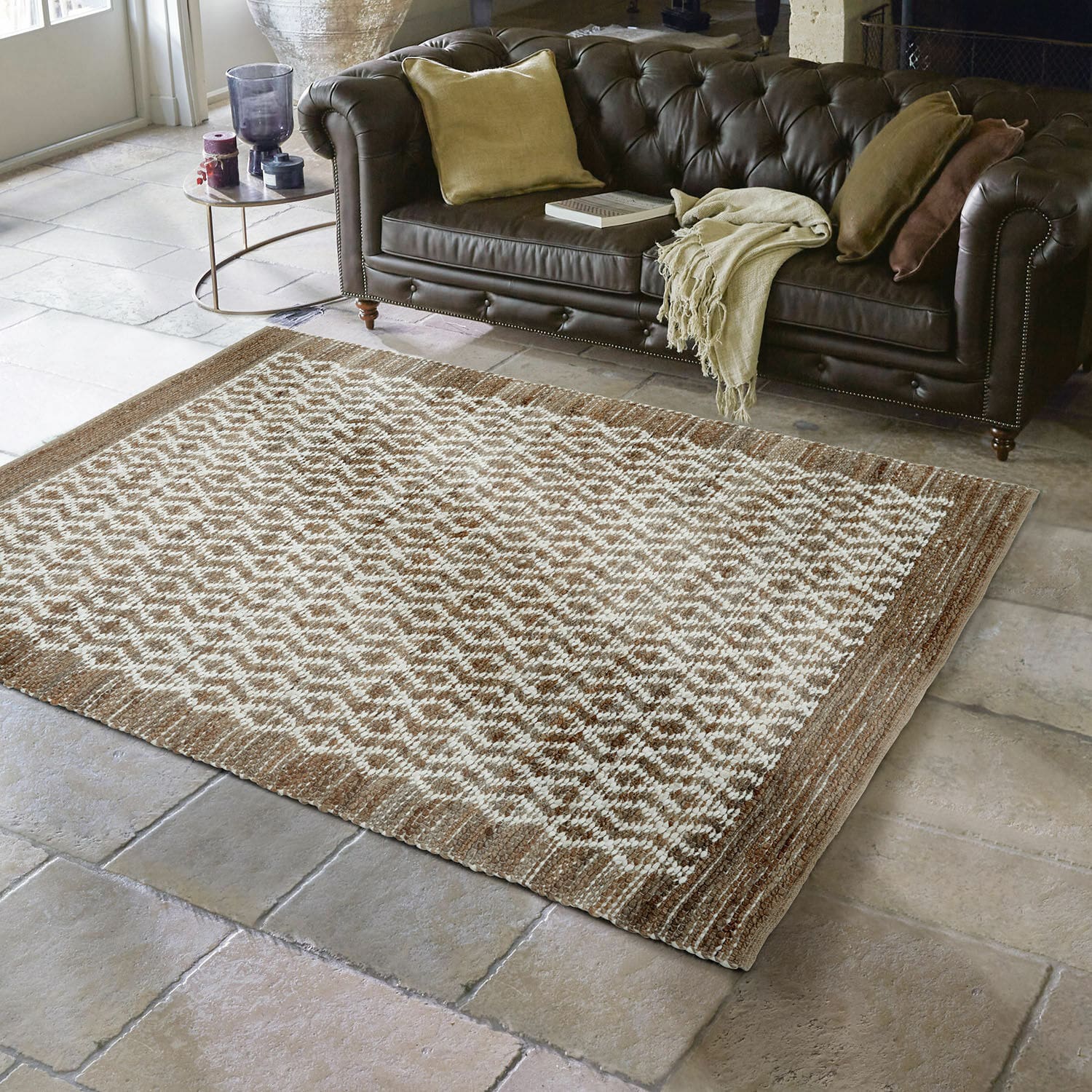 Wendeteppich Amhara Braun-cremefarbener Teppich mit geometrischem Muster auf Steinboden vor dunklem Ledersofa im Wohnzimmer