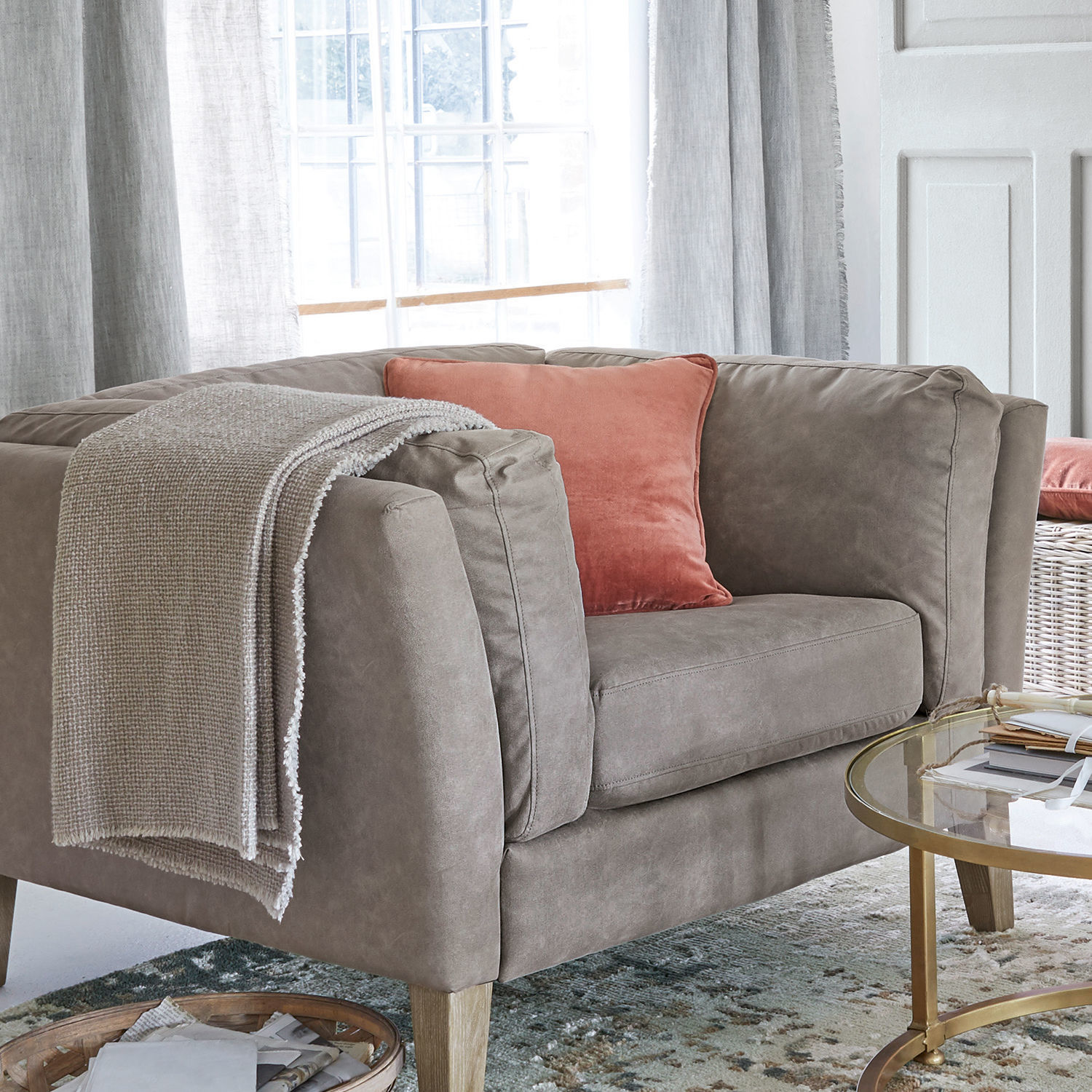 Graues Stoffsofa mit orangefarbenem Kissen und beiger Decke in hellem Wohnzimmer mit Fenster