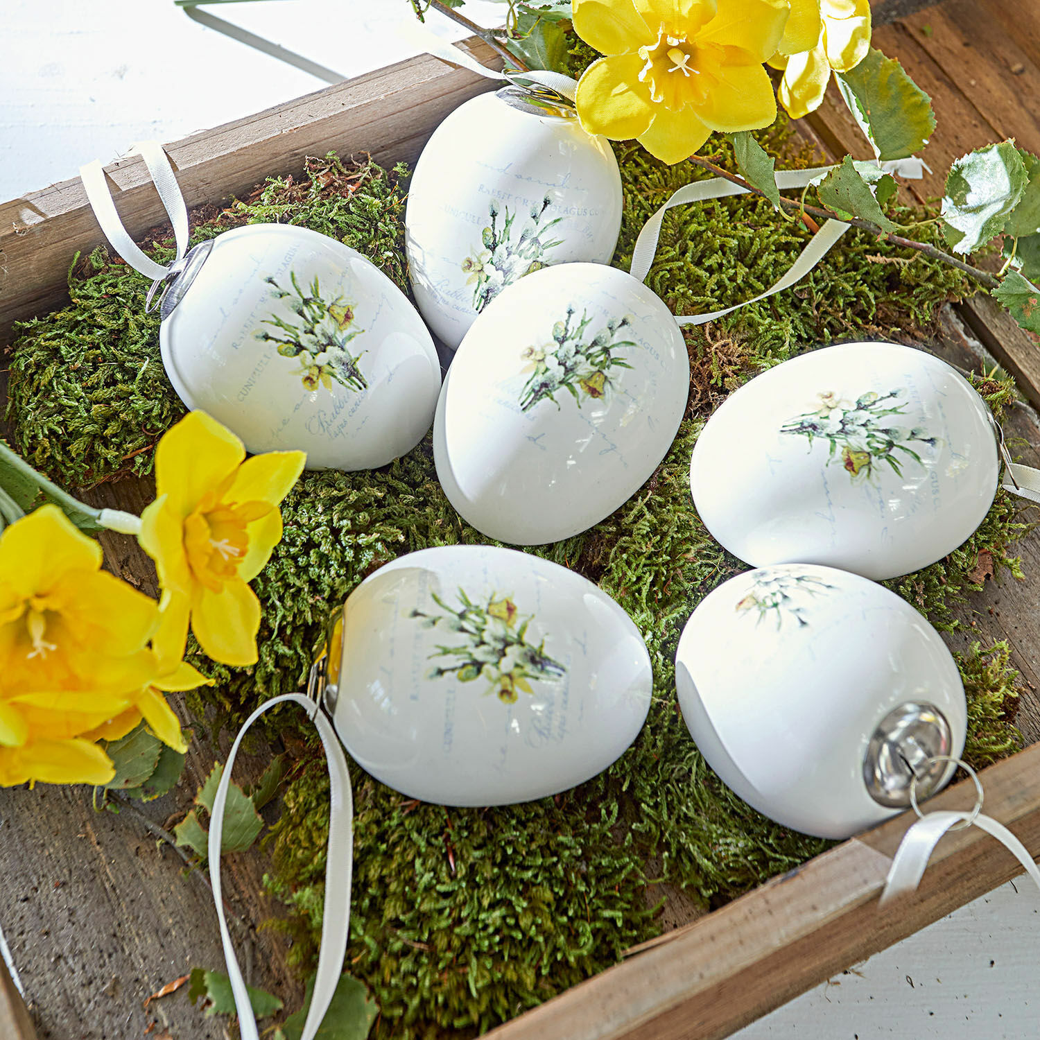 Weiße Keramik-Ostereier mit Blumenmotiv auf grünem Moos, frühlingshafte Dekoration
