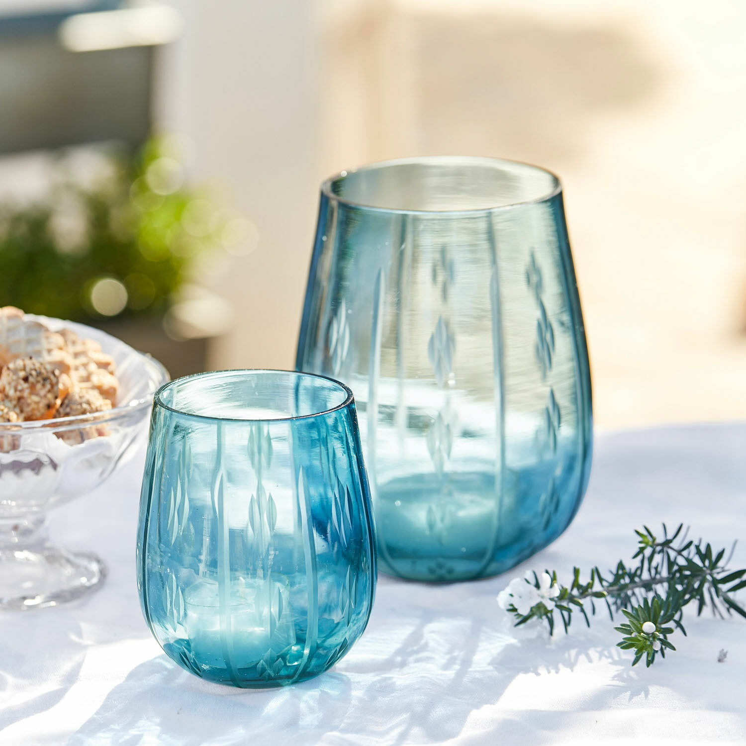 Zwei blaue Glaswindlichter mit graviertem Muster auf weißem Hintergrund, Tischdekoration
