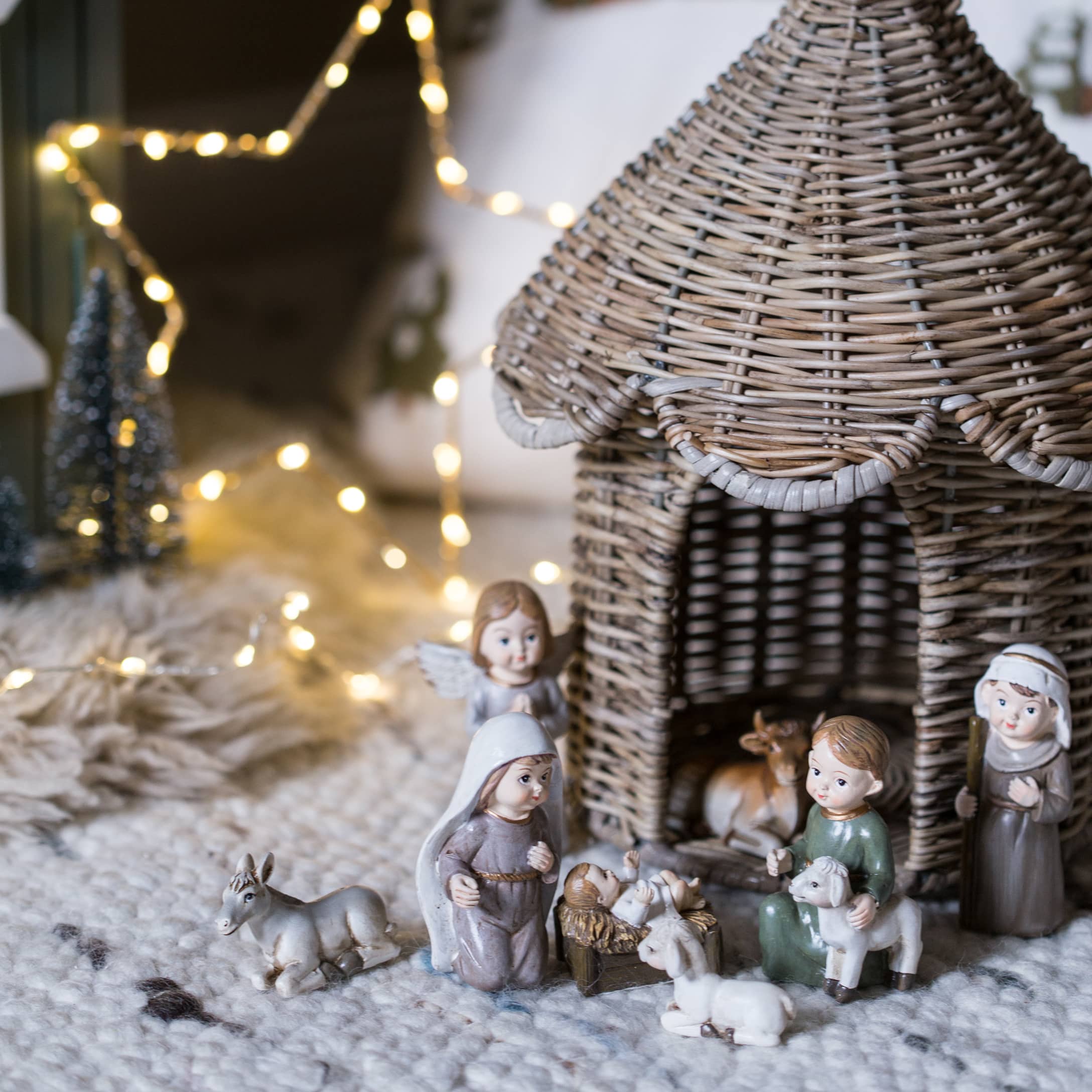 Weihnachtskrippenfiguren mit Korbhaus und Figuren auf weichem Teppich mit Lichterkette