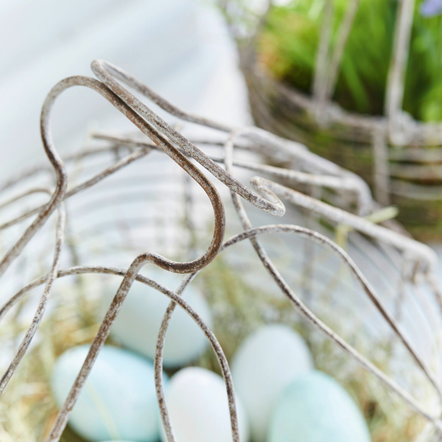 Korb aus patiniertem Metall mit blauen und weißen Dekoeiern für Ostern