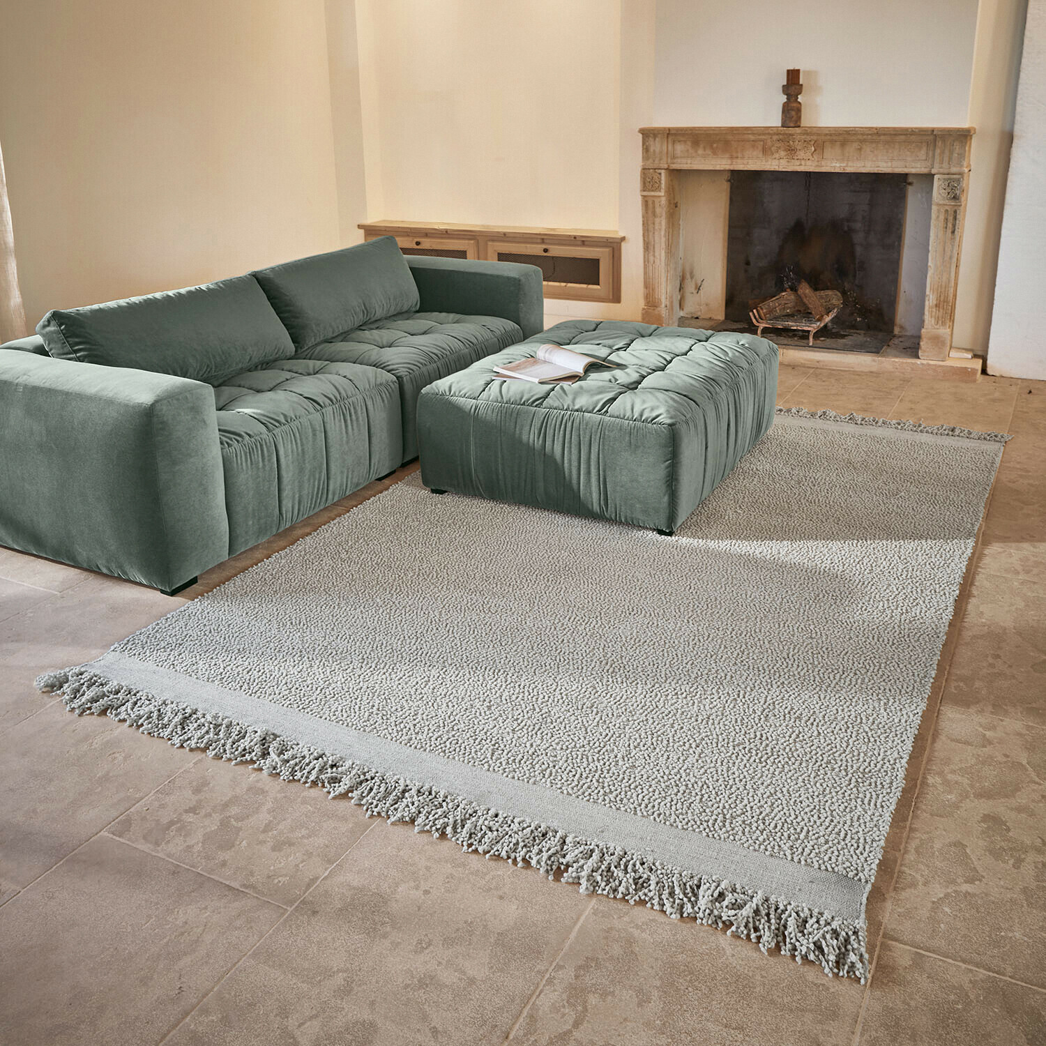 Teppich Linnet Grünes Samtsofa mit gesteppter Sitzfläche und passendem Hocker auf hellem Teppich vor Kamin