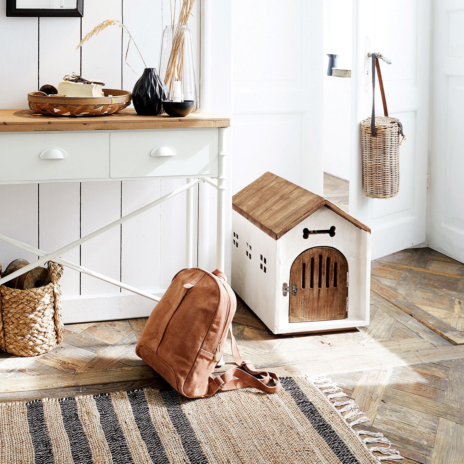 Holz-Hundehütte in Weiß und Braun auf Holzboden mit braunem Rucksack und gestreiftem Teppich