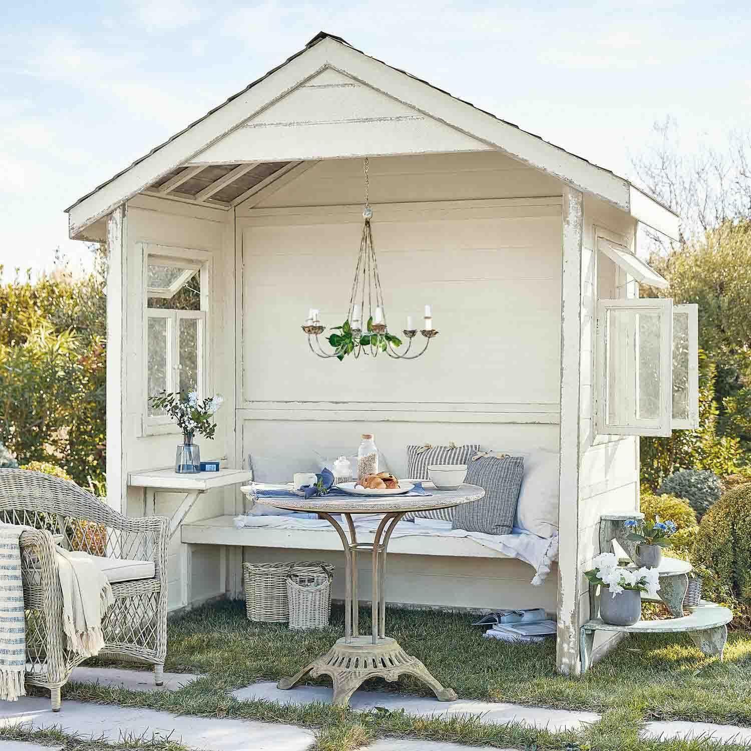 Weißes Holz-Gartenhaus mit Korbsessel und rundem Tisch auf Rasenfläche