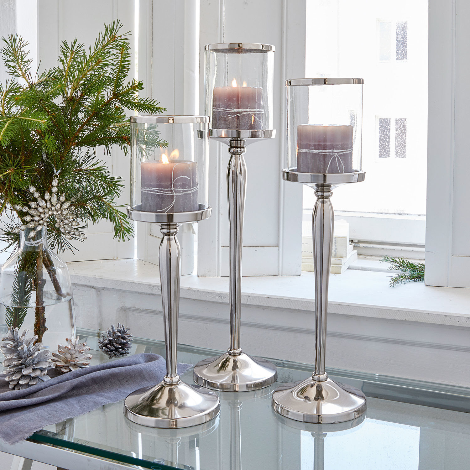 Kerzenständer 3er Set Serres Drei silberne Kerzenhalter aus Glas und Metall mit violetten Kerzen auf Glastisch