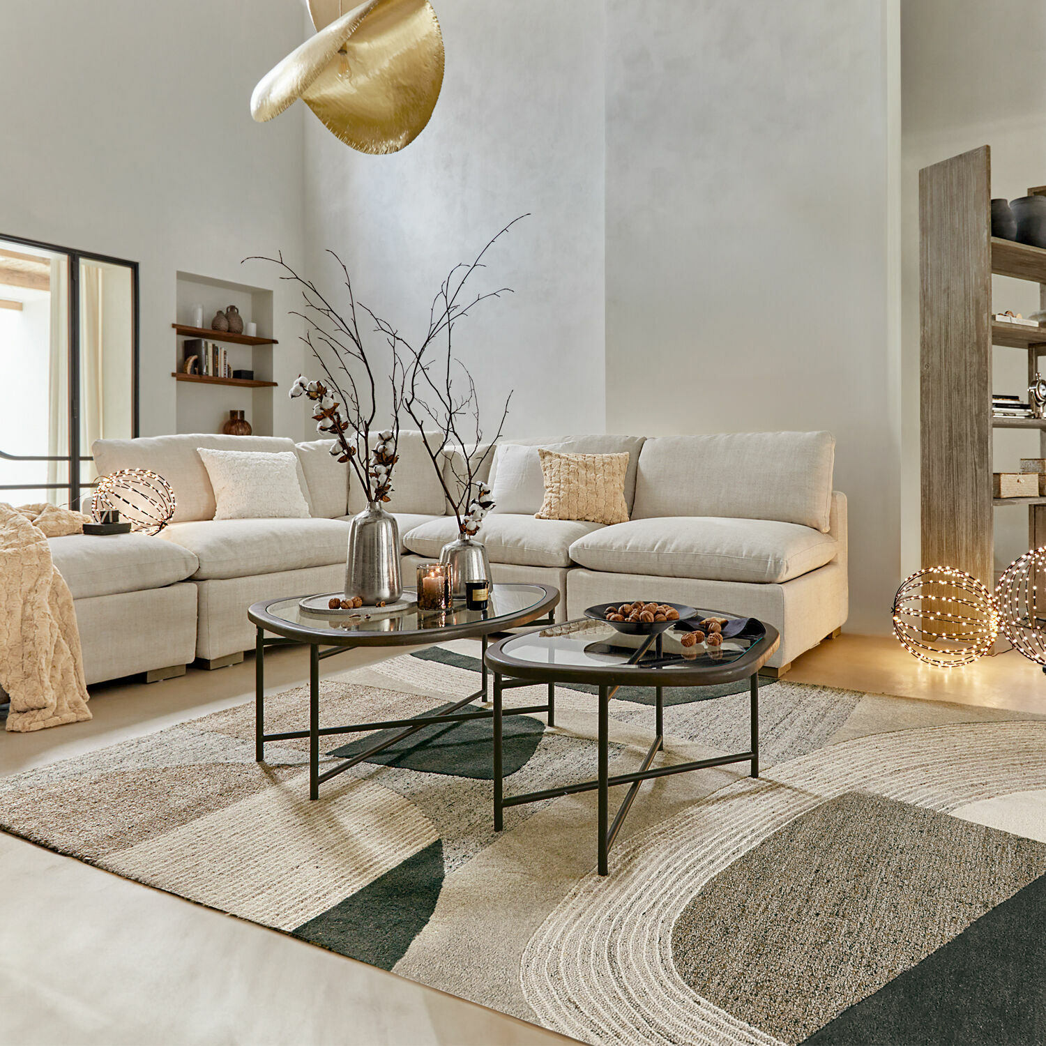 Modernes Wohnzimmer mit beigem Sofa, gläsernen Couchtischen und geometrischem Teppich in neutralen Farben
