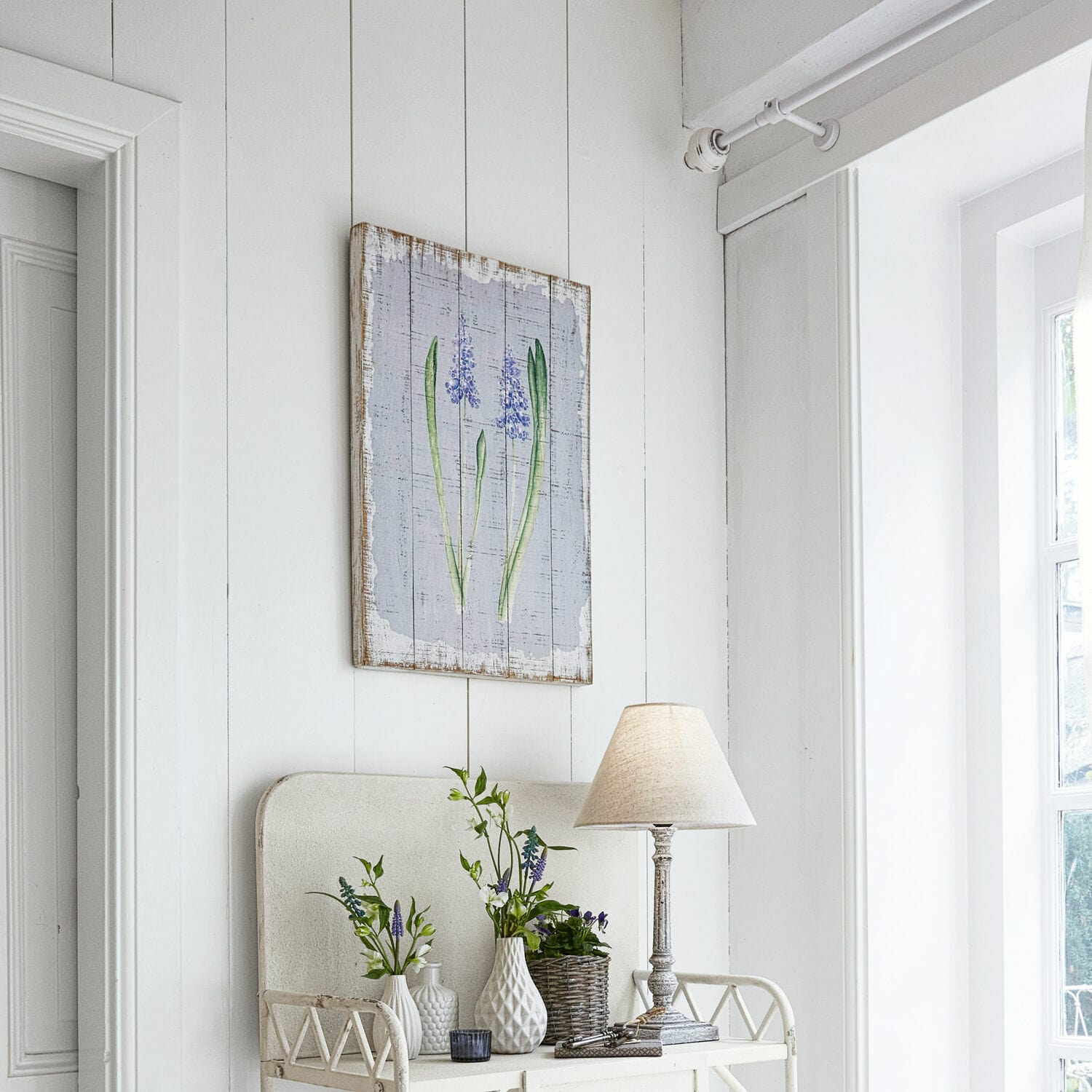 Dekoratives Holzbild mit lila Blumenmotiv in hellem Raum mit Lampe und Vasen