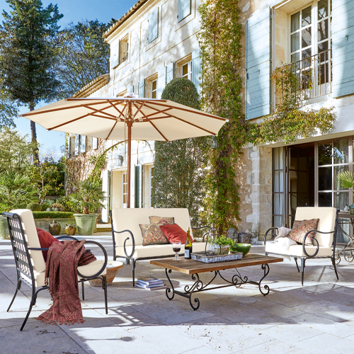 Gartenmöbel-Set mit Metallrahmen und cremefarbenen Polstern auf Stein-Terrasse mit Sonnenschirm