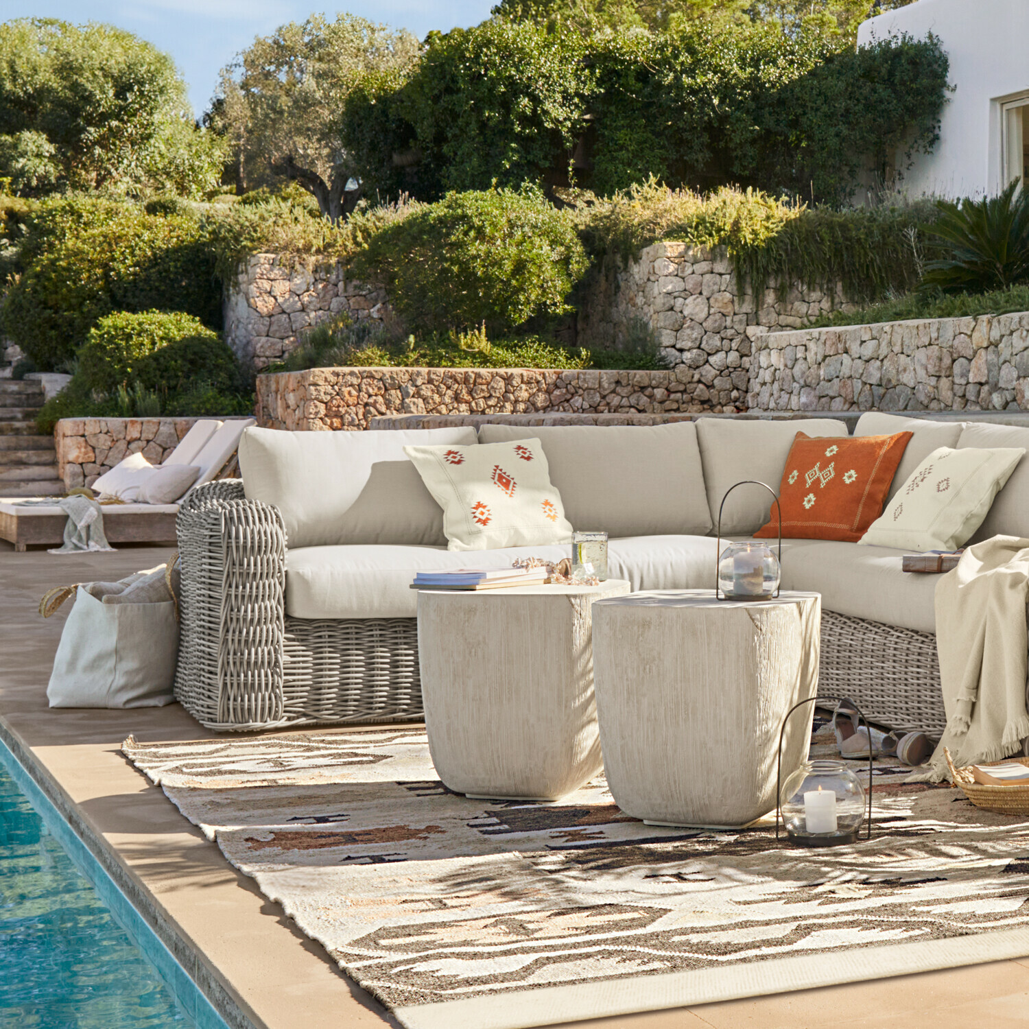 Gartensitzgruppe mit grauem Rattan-Ecksofa und cremefarbenen Kissen neben dem Pool