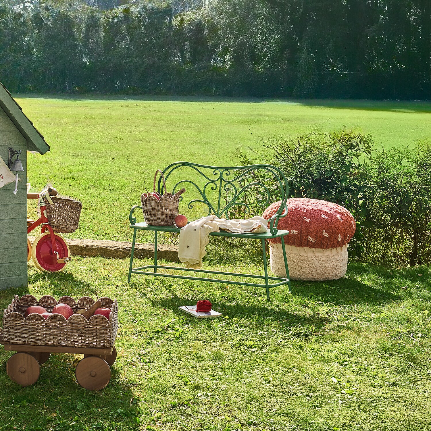 Grüne Metall-Gartenbank mit Korb und rotem Pilz-förmigem Sitzpouf auf Gras im Garten