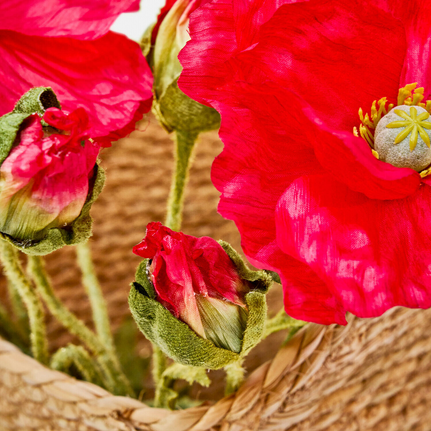Rote künstliche Mohnblumen mit grünen Knospen in einem Korb aus Weide, Wohnraumdekoration