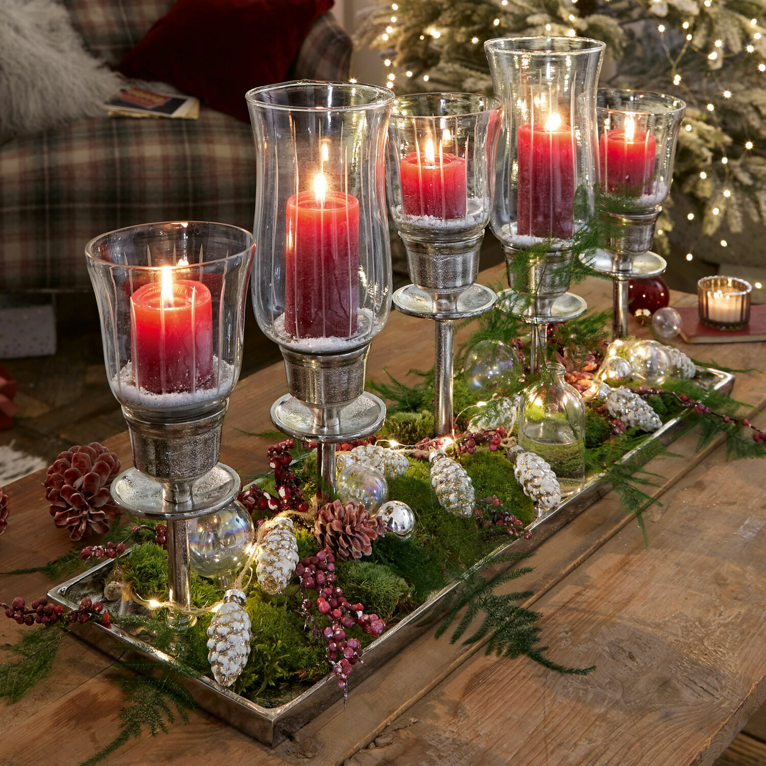 Dekorativer Glas-Metall-Kerzenhalter mit roten Kerzen und Weihnachtsdeko auf Holztisch