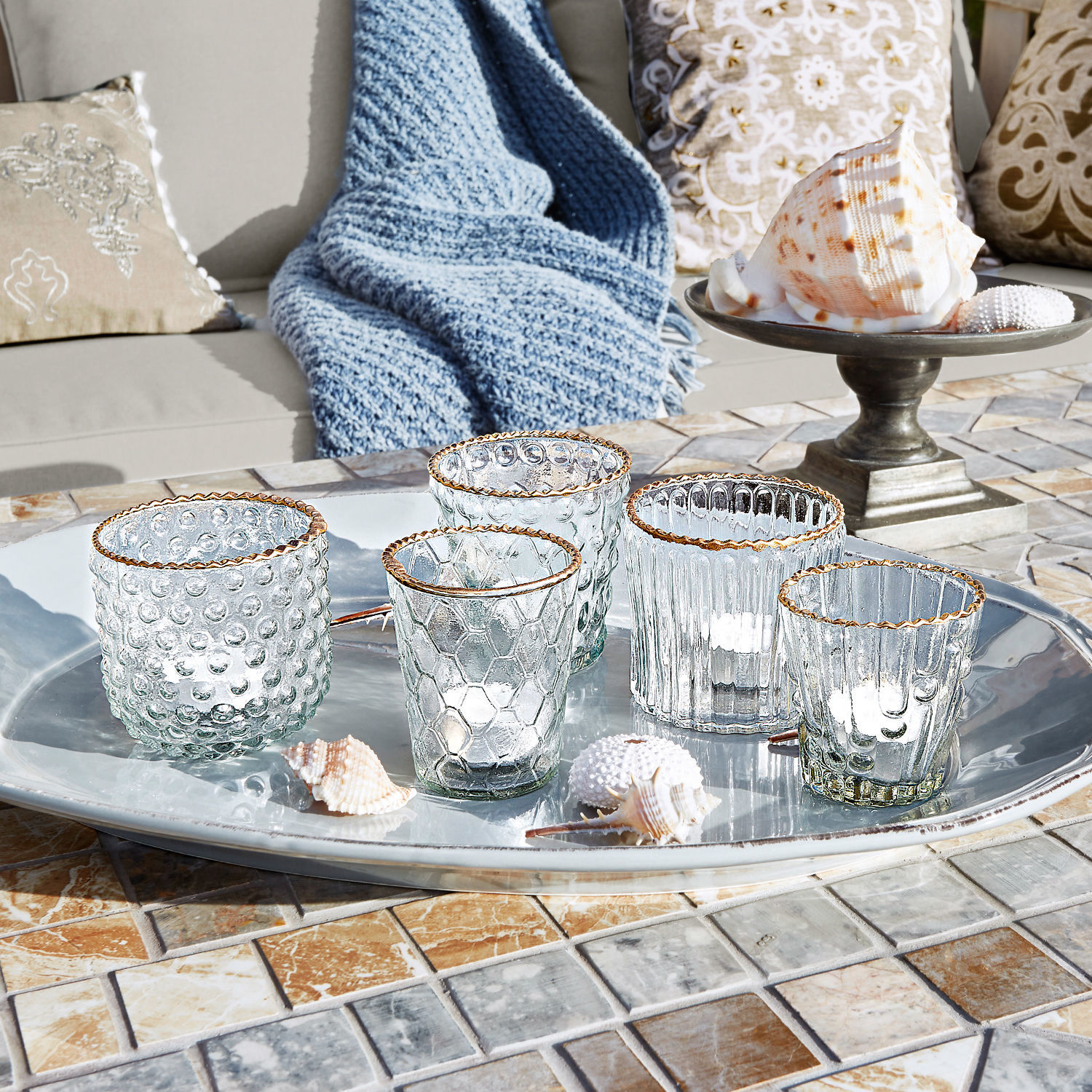 Fünf Glas-Teelichthalter mit goldfarbenem Rand auf silbernem Tablett auf Mosaiktisch