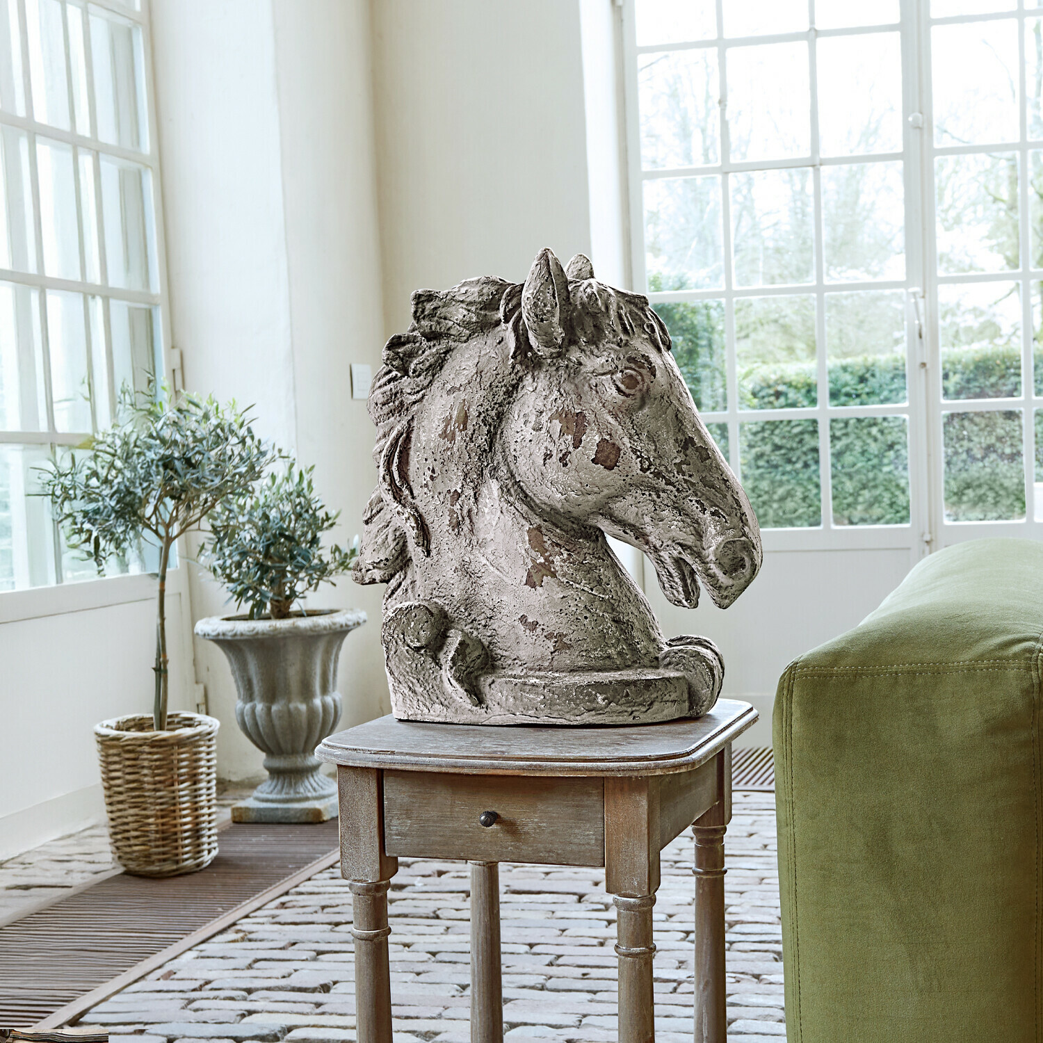 Deko-Pferd Ghenire Skulptur eines Pferdekopfes aus antik wirkendem Stein auf Holzbeistelltisch neben grünem Sofa mit Kissen