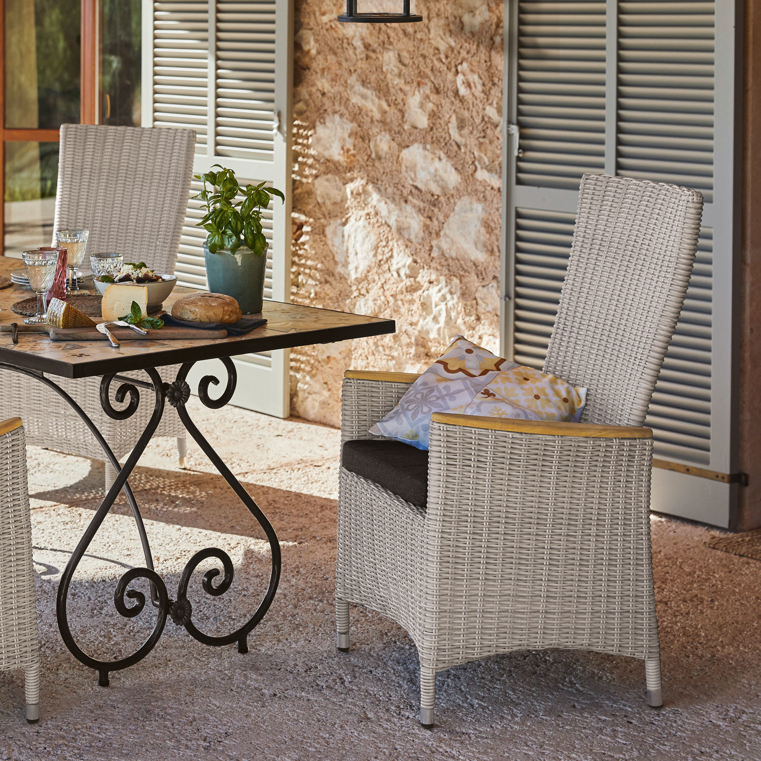 Hellgrauer Rattanstuhl mit Kissen und Metalltisch auf Terrasse, Gartenmöbel