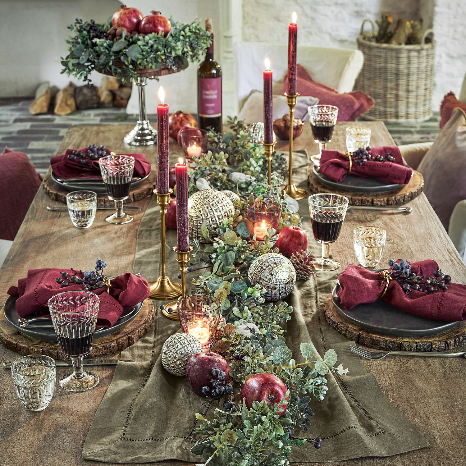 Rustikaler Tisch mit grünem Läufer, roten Kerzen und Dekoration aus Früchten und Blättern für Festtafel