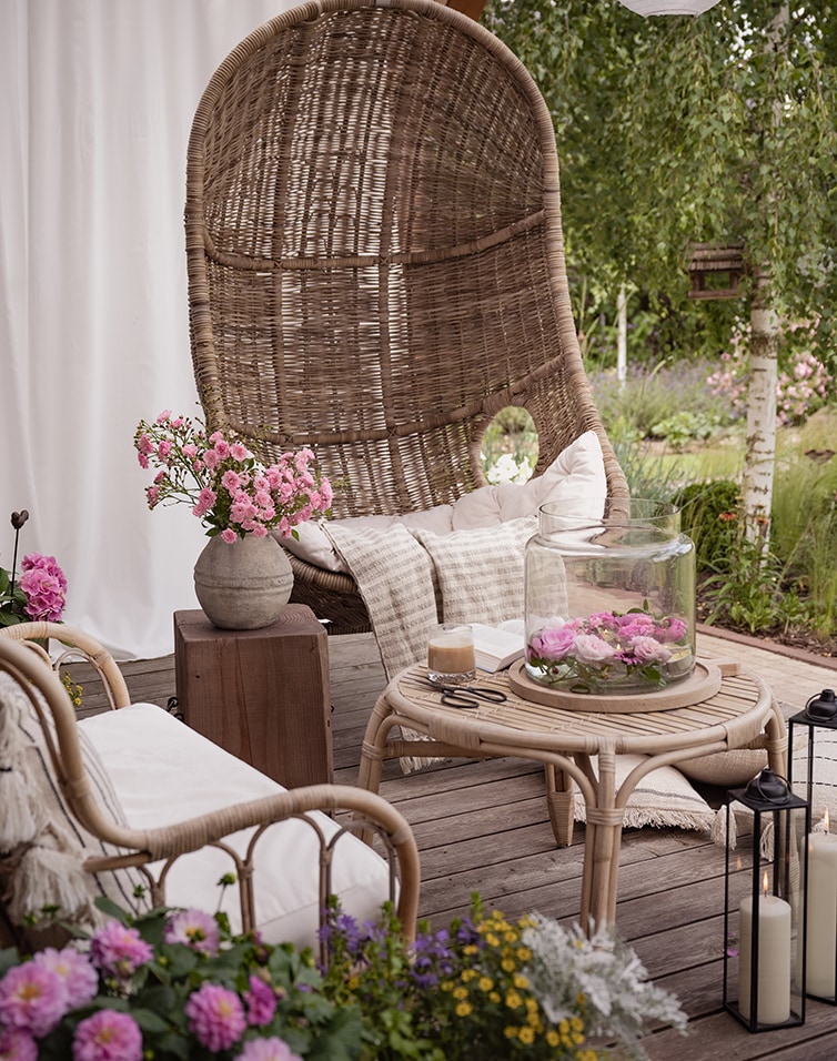 Gemütliche Sitzecke mit Rattansessel und Beistelltisch auf Terrasse mit Blumen und Kerzen