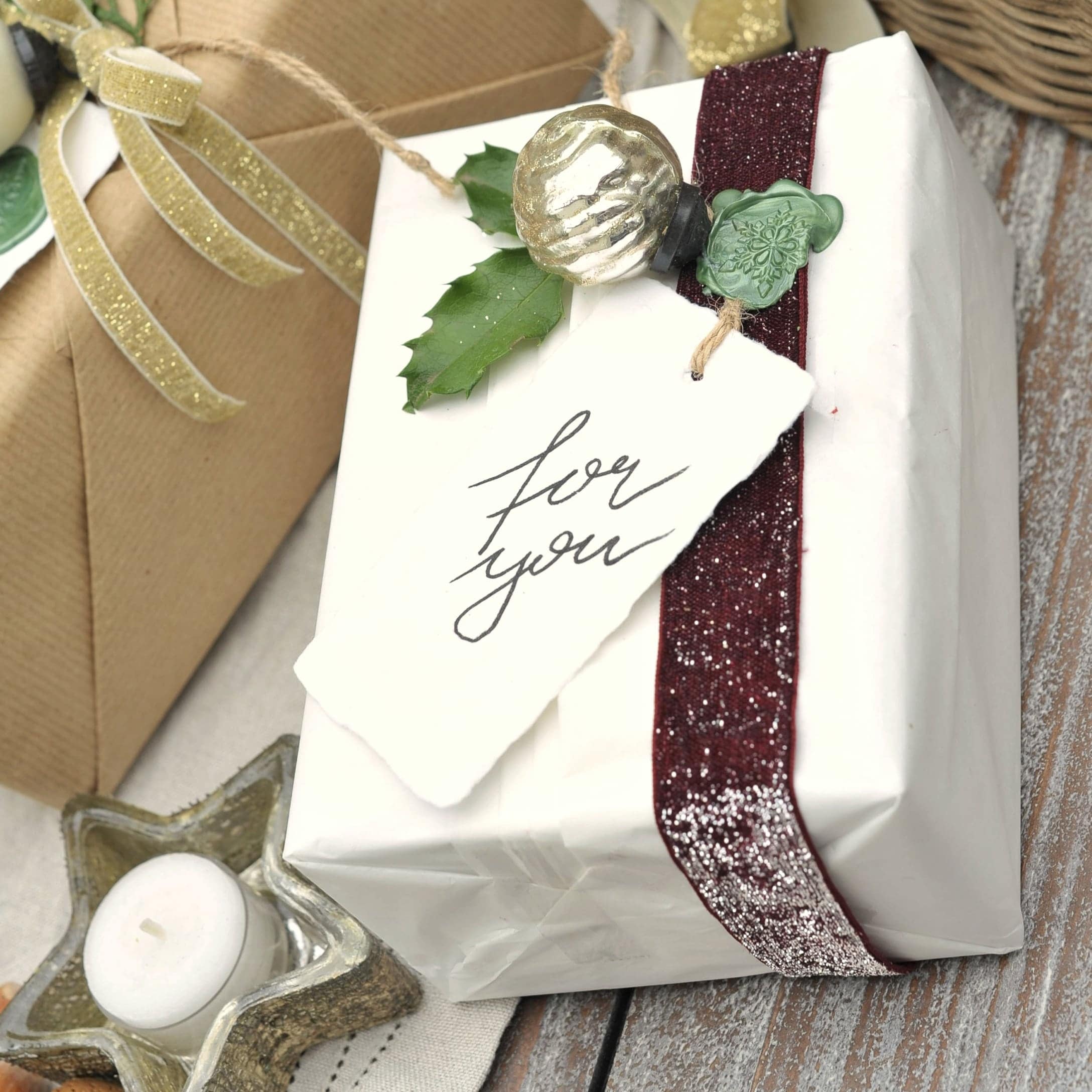 Weiß verpacktes Geschenk mit bordeauxrotem Band und grünem Stechpalmenblatt als Dekoration