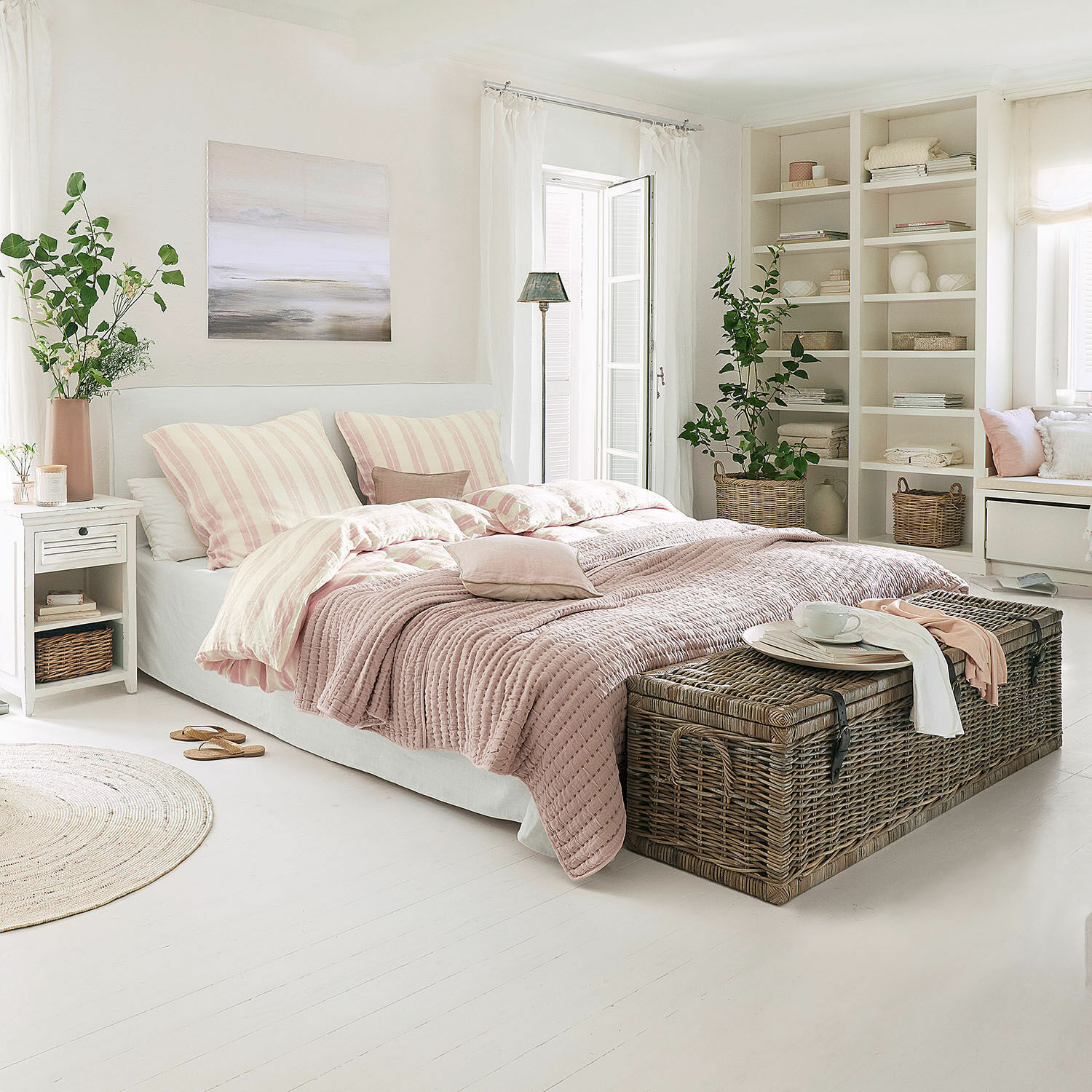 Gemütliches Schlafzimmer mit Bett in rosa Bettwäsche und Korbtruhe auf weißem Boden