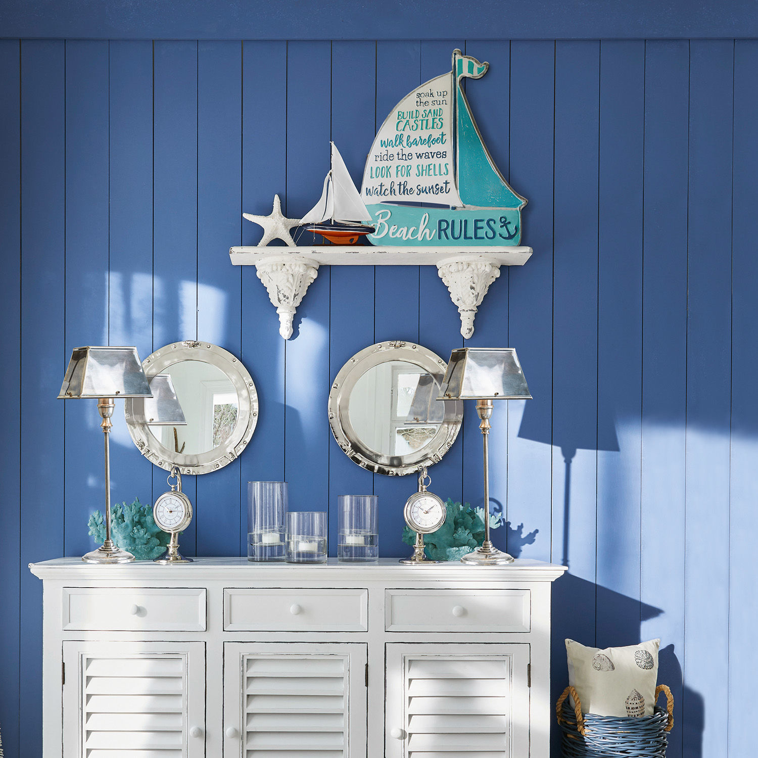 Weißes Holzsideboard mit Stranddeko und zwei runden Spiegeln an blauer Wand