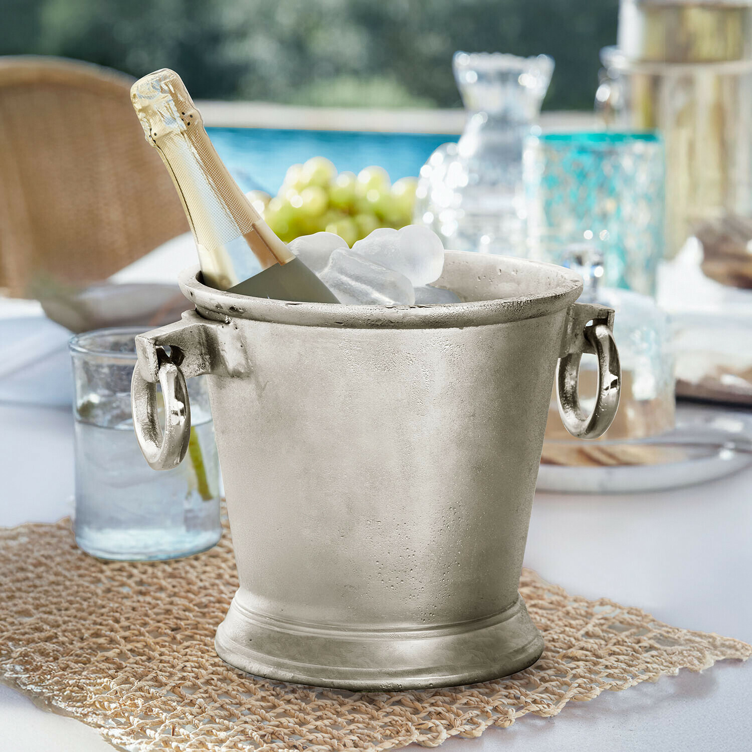 Silberner Metall-Eiswürfeleimer mit Champagnerflasche und Eis auf Gartentisch