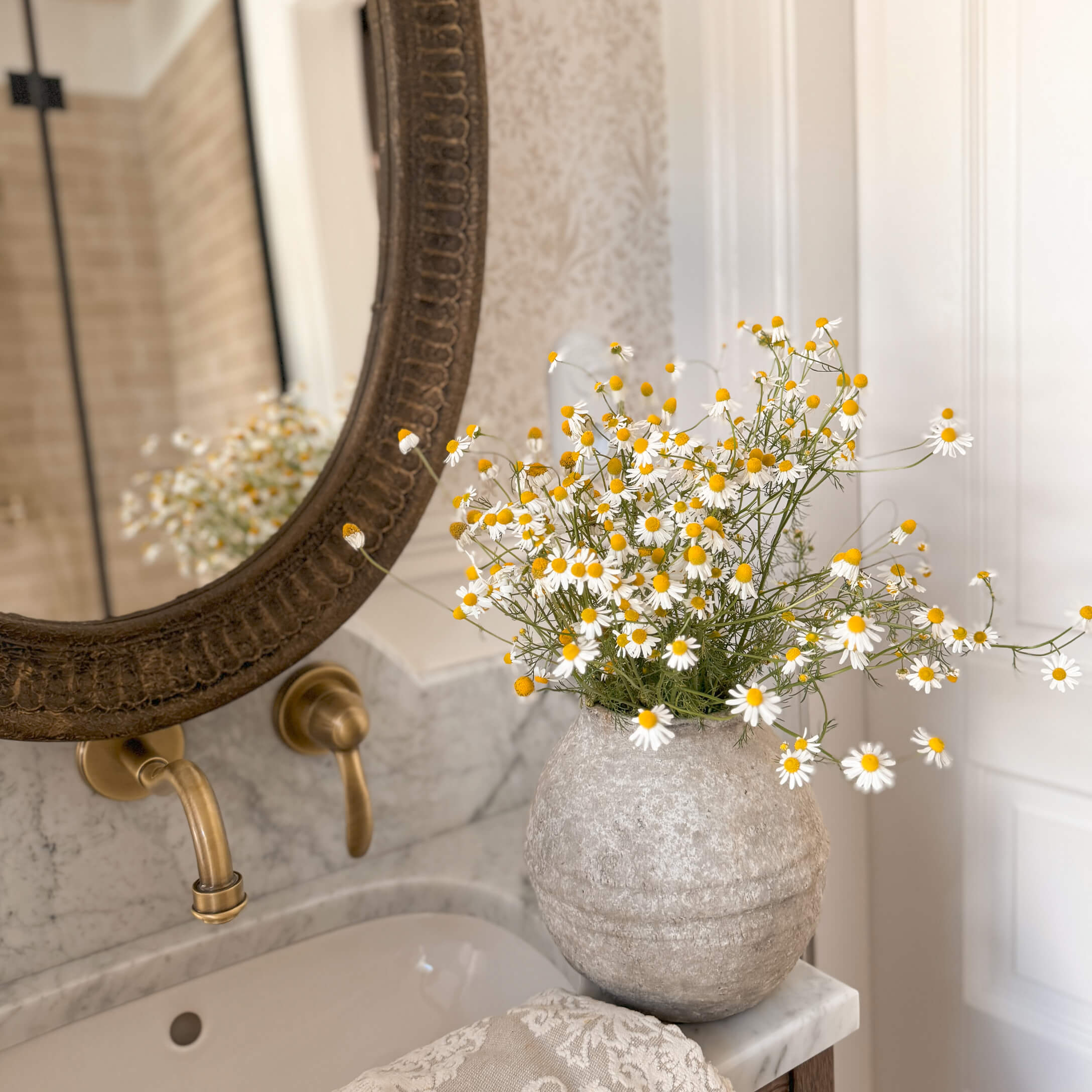 Graue Steinvase mit weißen und gelben Blumen auf Marmorwaschbecken in elegantem Badezimmer