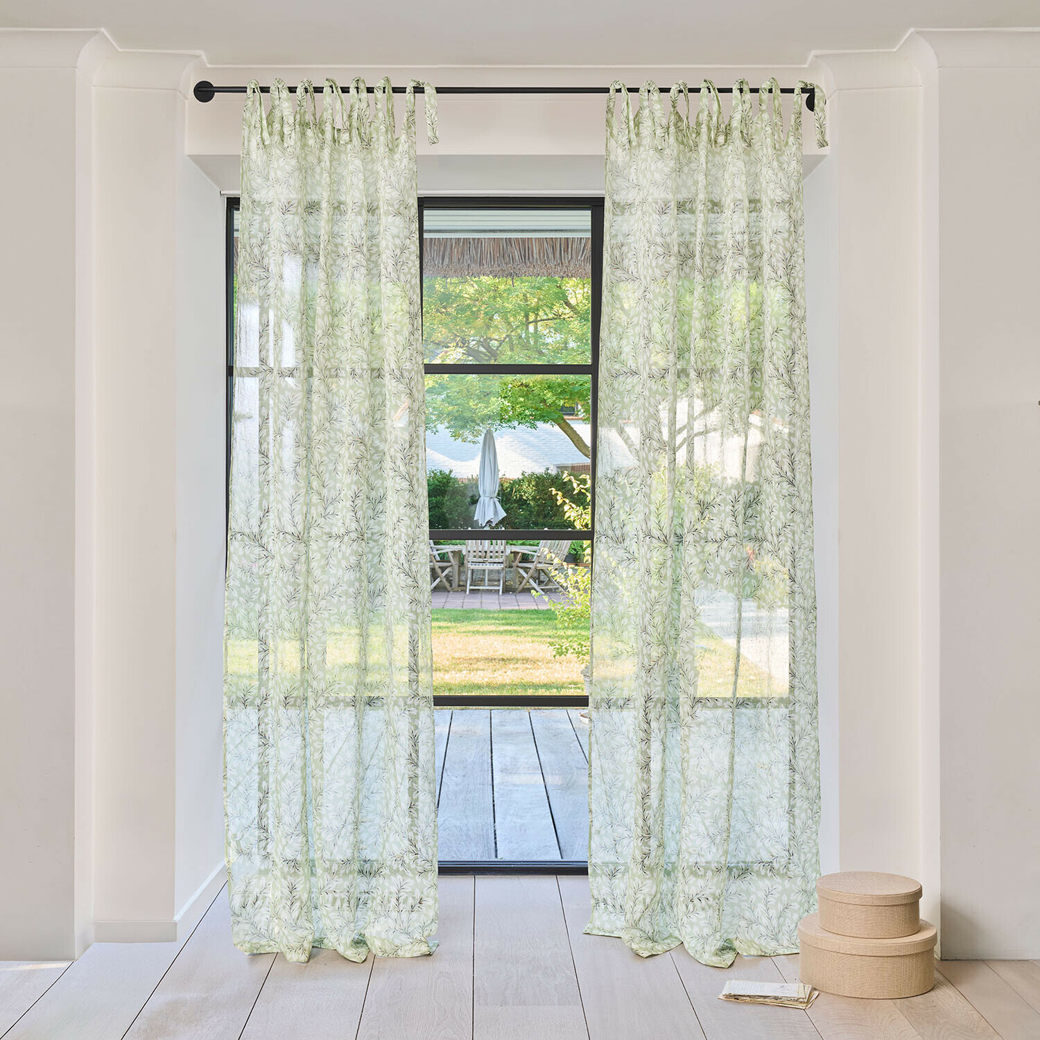 Gardine Norelline Transparente Vorhänge mit grünem Blattmuster an schwarzer Gardinenstange in hellem Raum mit Gartenblick