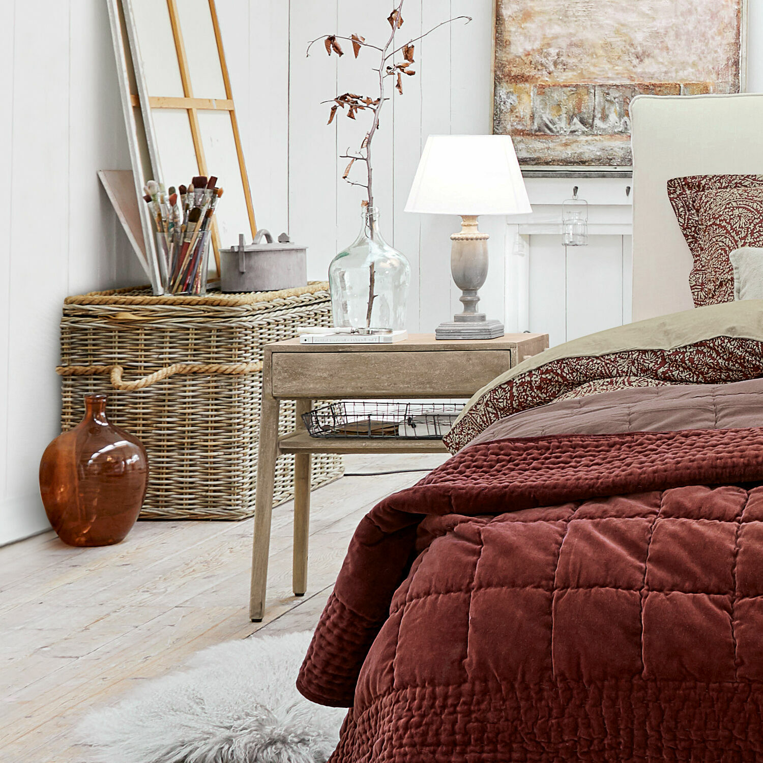 Gemütliches Schlafzimmer mit bordeauxroter Steppdecke und Holz-Nachttisch auf hellem Boden