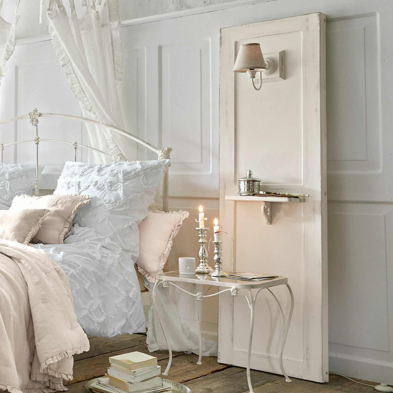 Weißes Metallbett mit weißer und beiger Bettwäsche, Nachttisch mit Kerzen und Wandlampe
