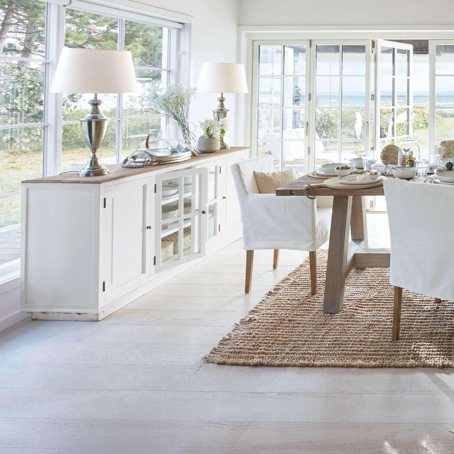 Helle Holzmöbel im Esszimmer mit weißen Stühlen und Naturteppich im skandinavischen Stil