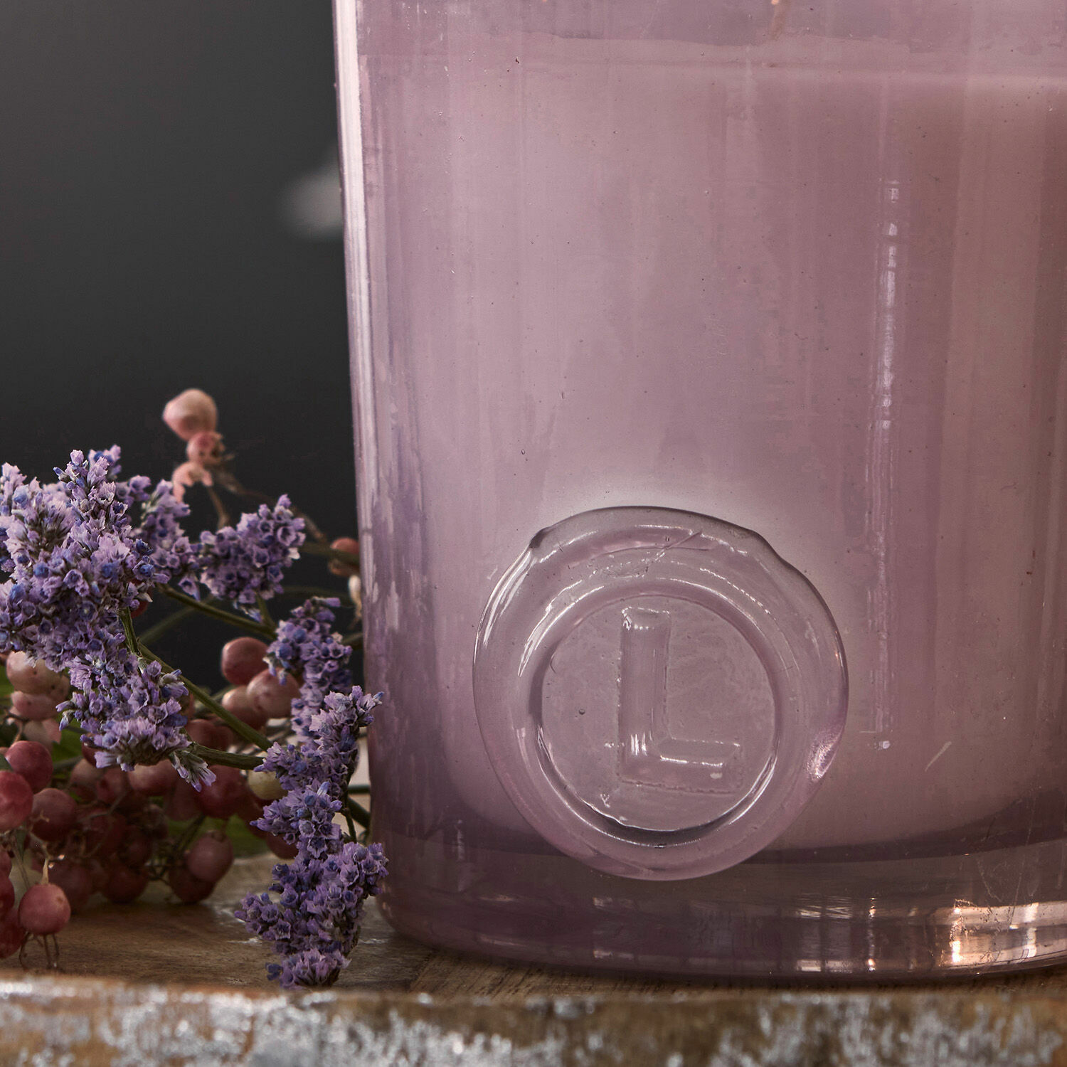 Violetter Glasvase mit L-Logo auf Holztisch mit Blumendekor, stilvolle Wohnaccessoire