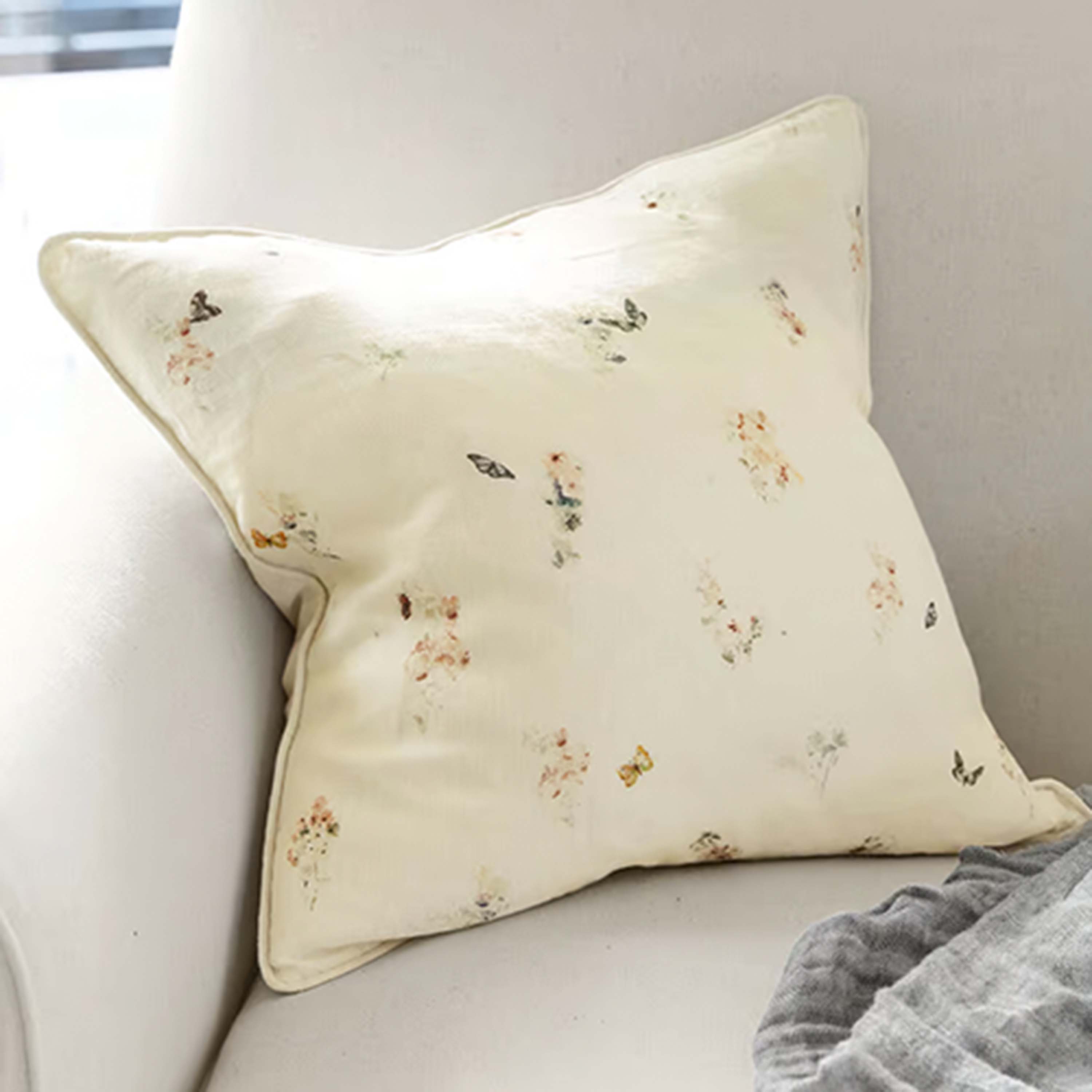Helles Dekokissen mit Schmetterlingsmuster auf beigem Stoff, ideal fürs Wohnzimmer