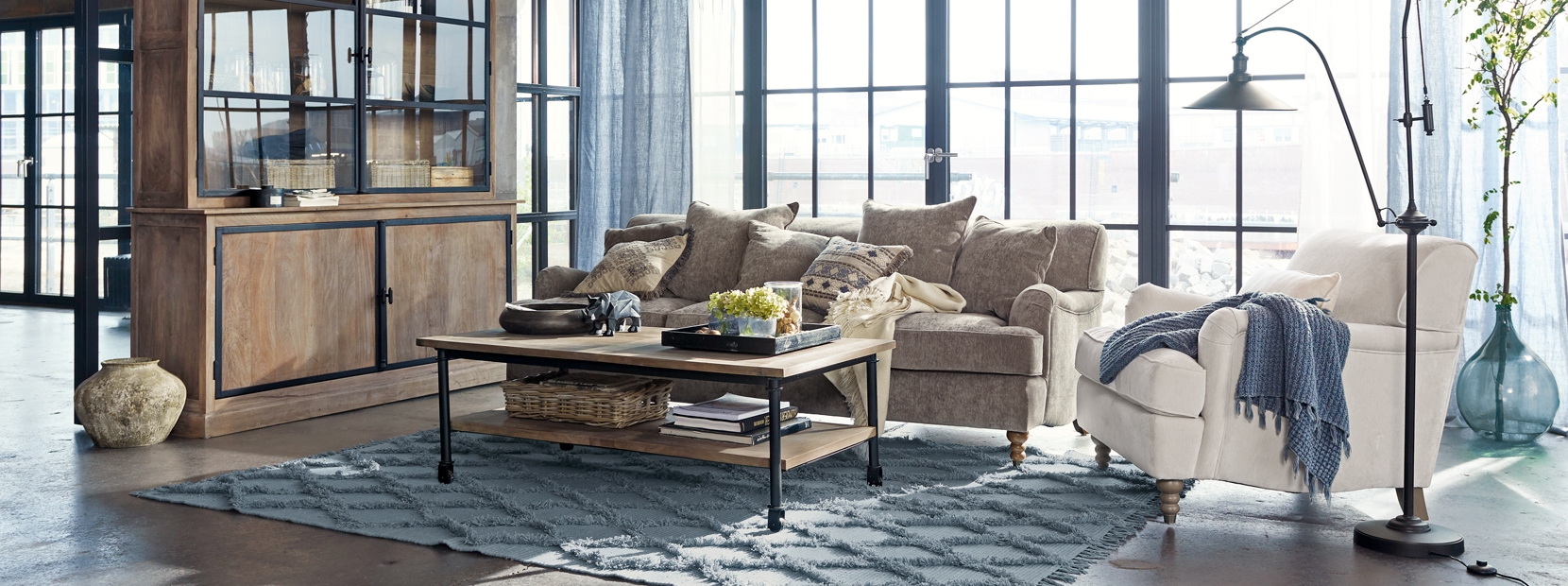 Industrielles Wohnzimmer mit Holzschrank, grauem Sofa und beigem Sessel auf blauem Teppich