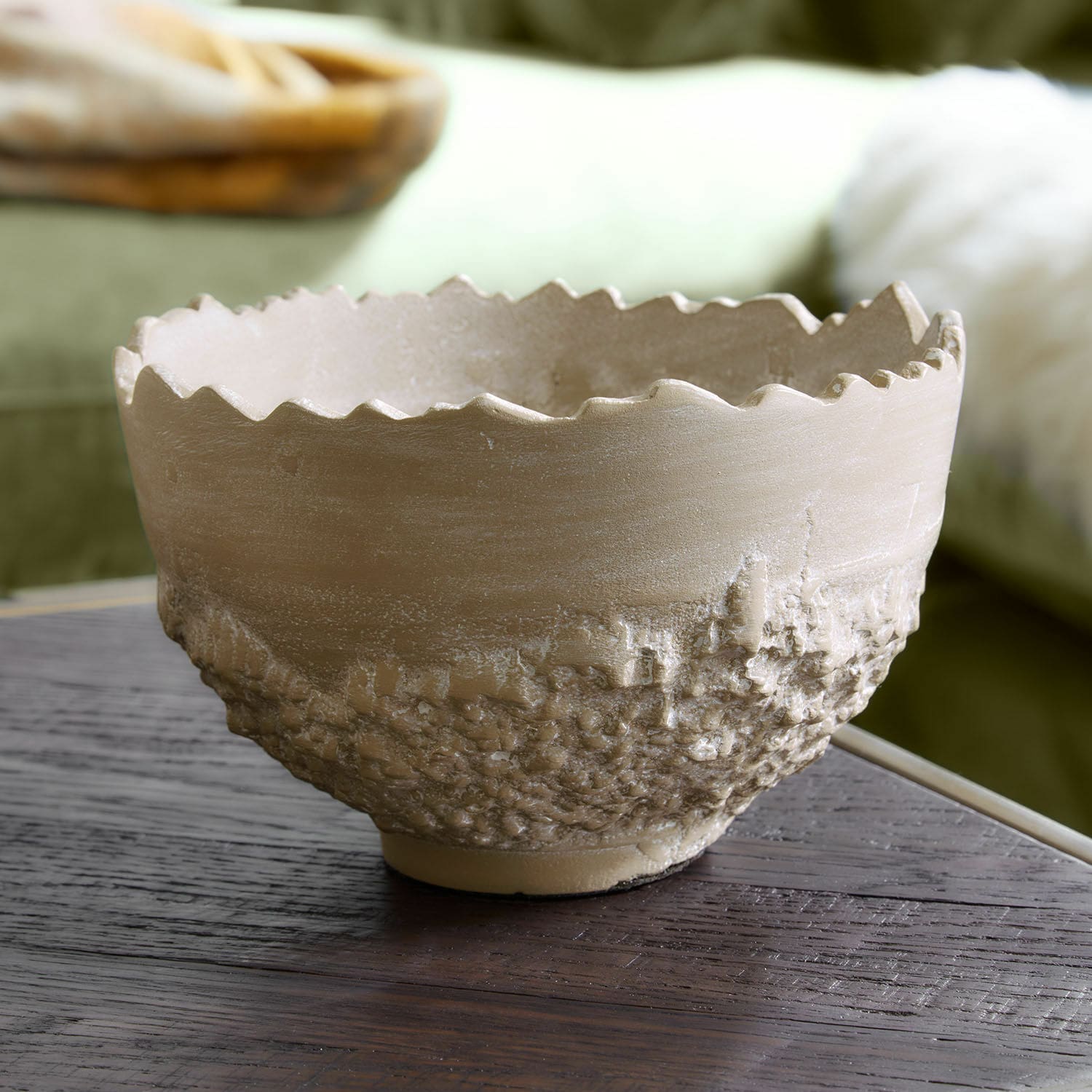 Beige Keramikschale mit rauer Struktur und welligem Rand auf dunklem Holztisch