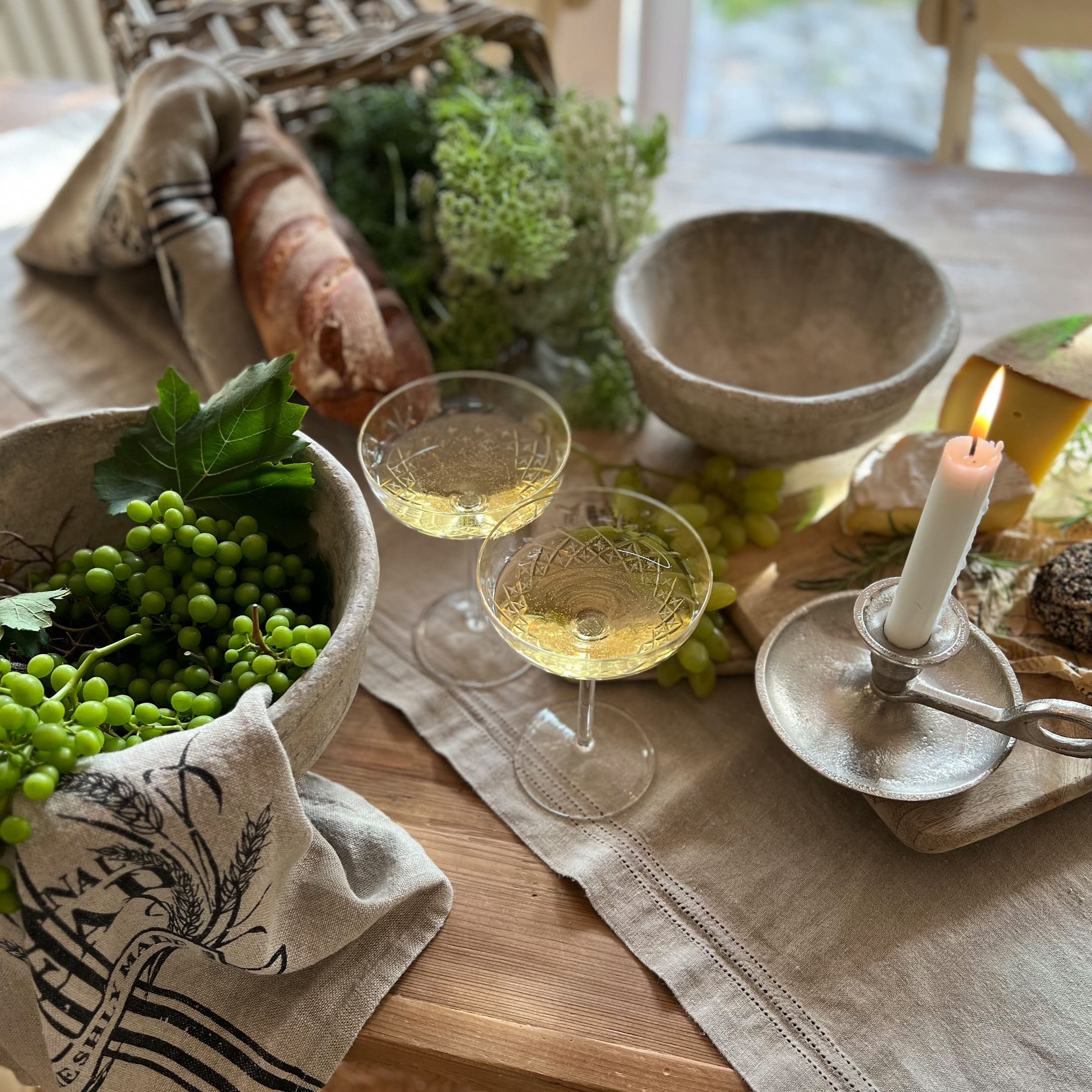 Rustikaler Holztisch mit Steinschalen, brennender Kerze, Weißweingläsern, Brot und grünen Trauben