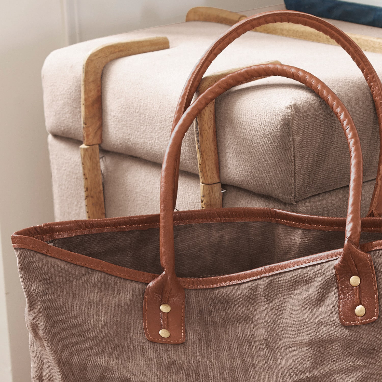 Braune Stofftasche mit braunen Ledergriffen vor beigem Möbelstück