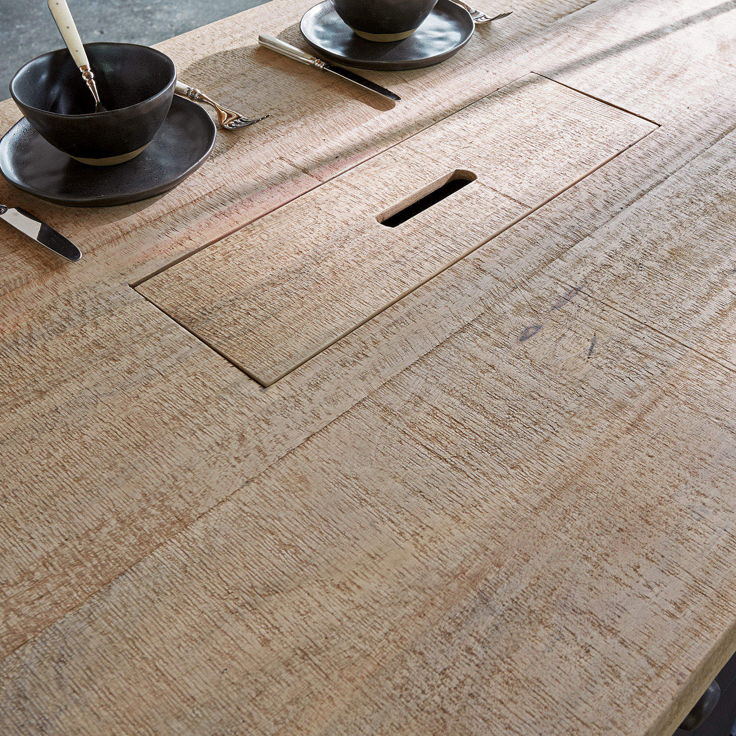 Tischplatte aus hellem Holz mit integriertem Fach und schwarzem Geschirr auf natürlichem Hintergrund