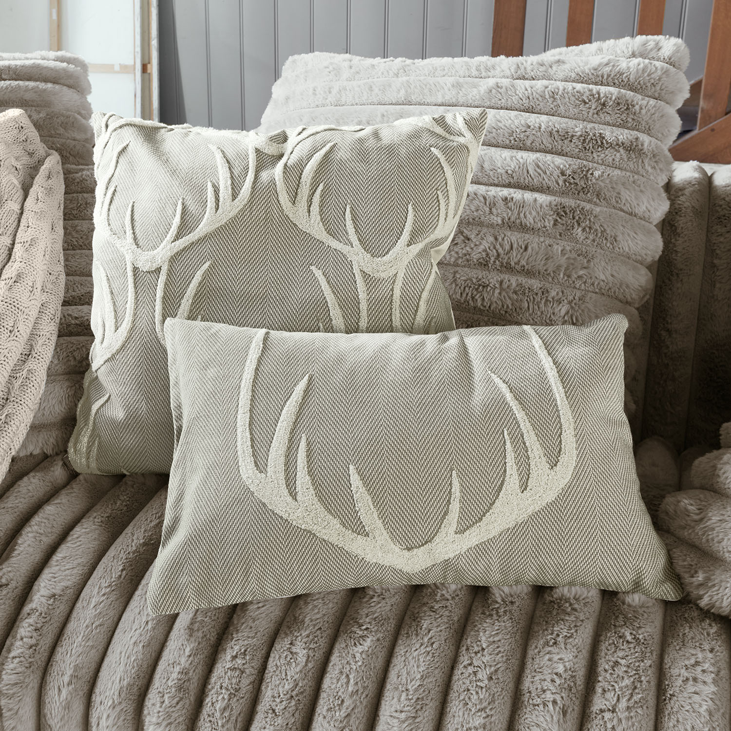 Beige Dekokissen mit Hirschgeweih-Motiv auf weichem Fellsofa, gemütliche Wohntextilien für Wohnzimmer