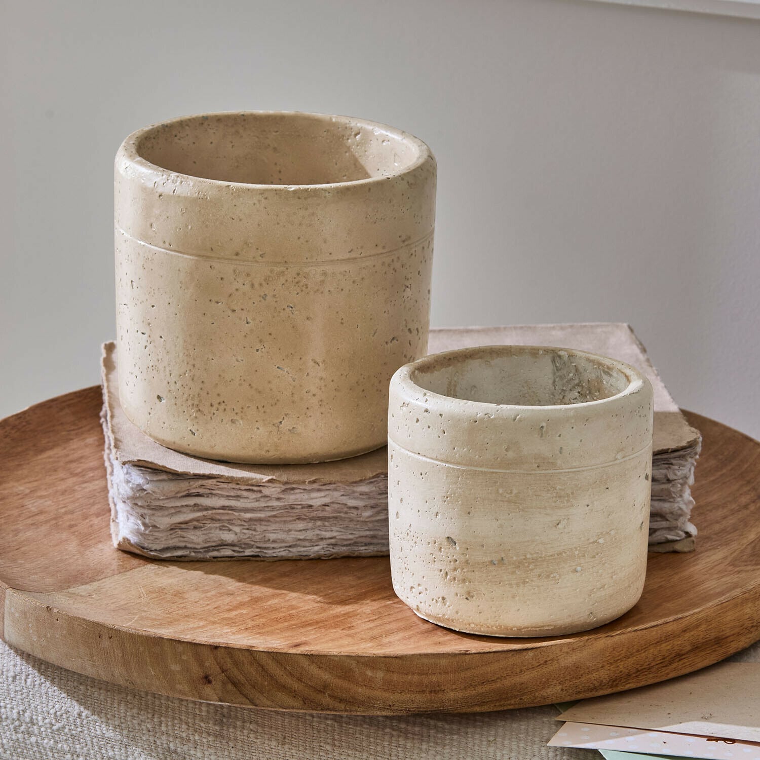 Zwei beige Betonblumentöpfe mit rauer Oberfläche auf einem Holztablett, Wohnaccessoire