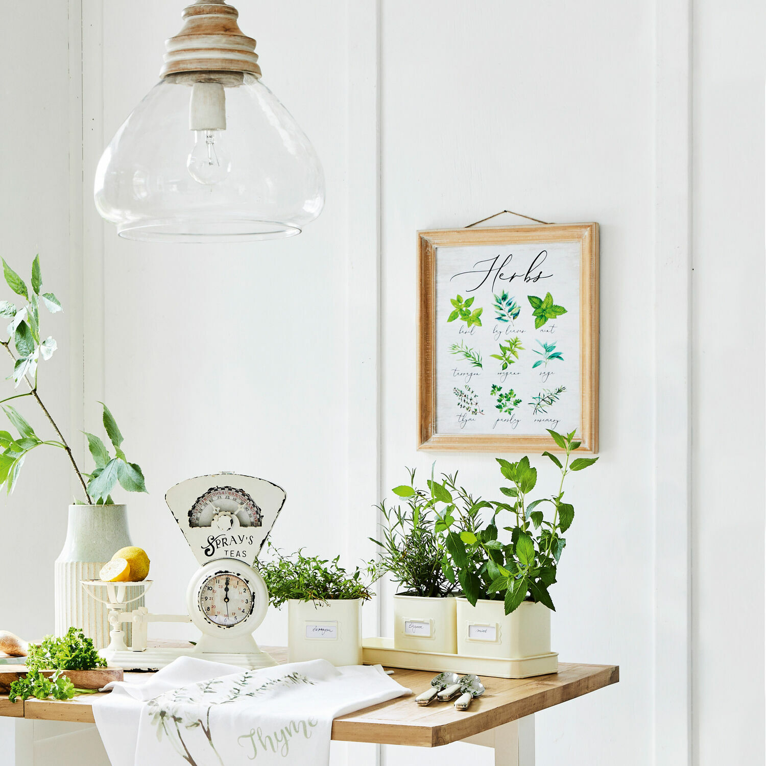 Helle Küche mit weißer Waage, Kräutertöpfen und hellem Holztisch im Landhausstil