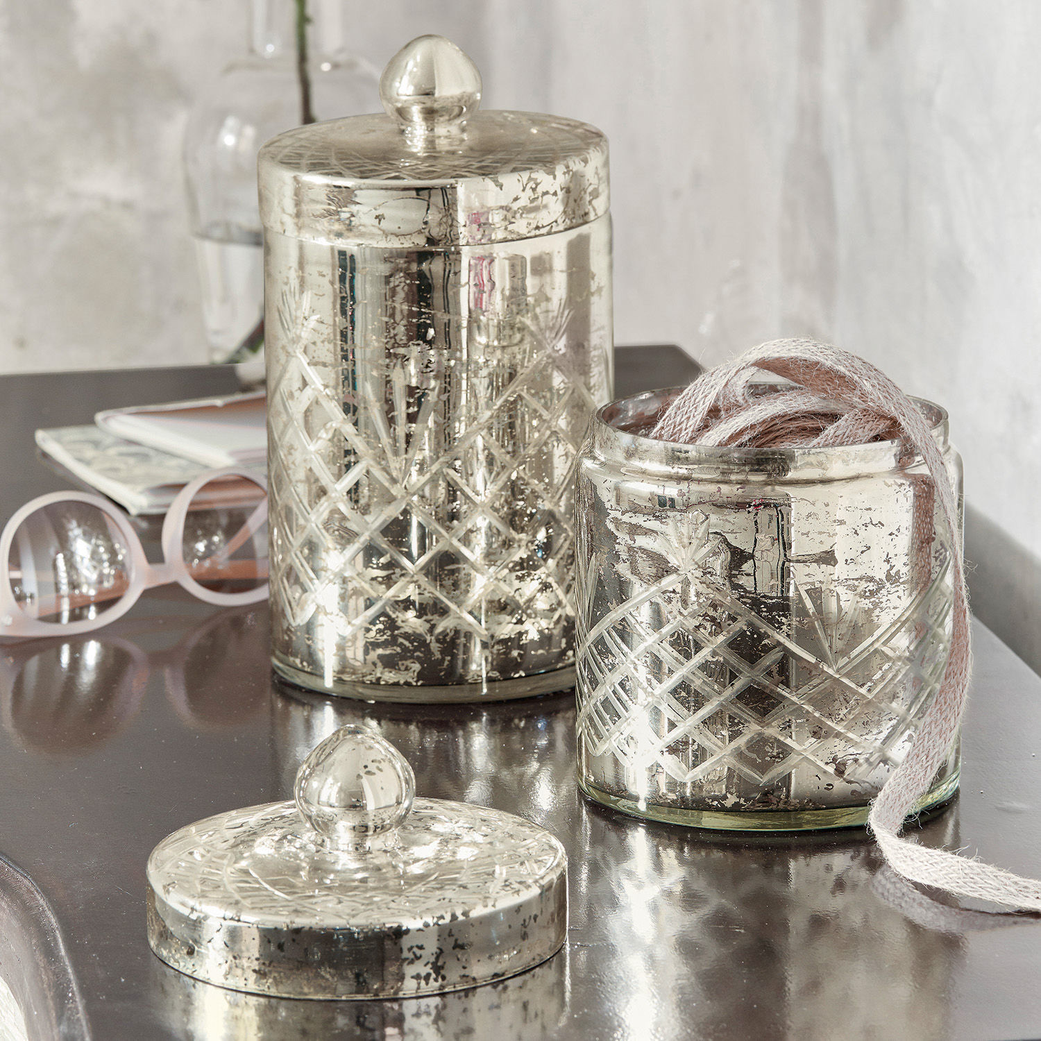 Dekorative Glasbehälter mit silberner Patina und graviertem Muster auf glänzendem Tisch