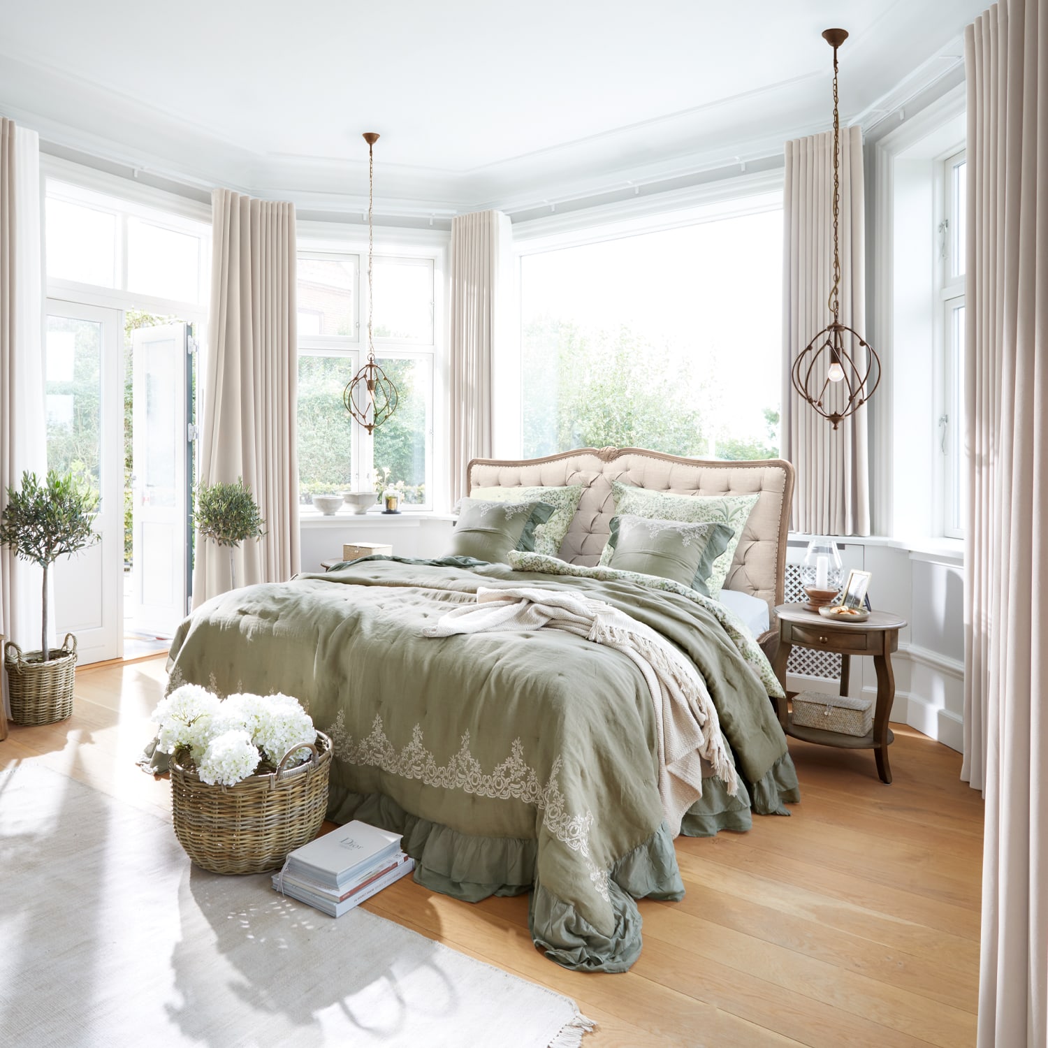Helles Schlafzimmer mit beige gepolstertem Bett, grüner bestickter Bettwäsche und hellem Holzboden