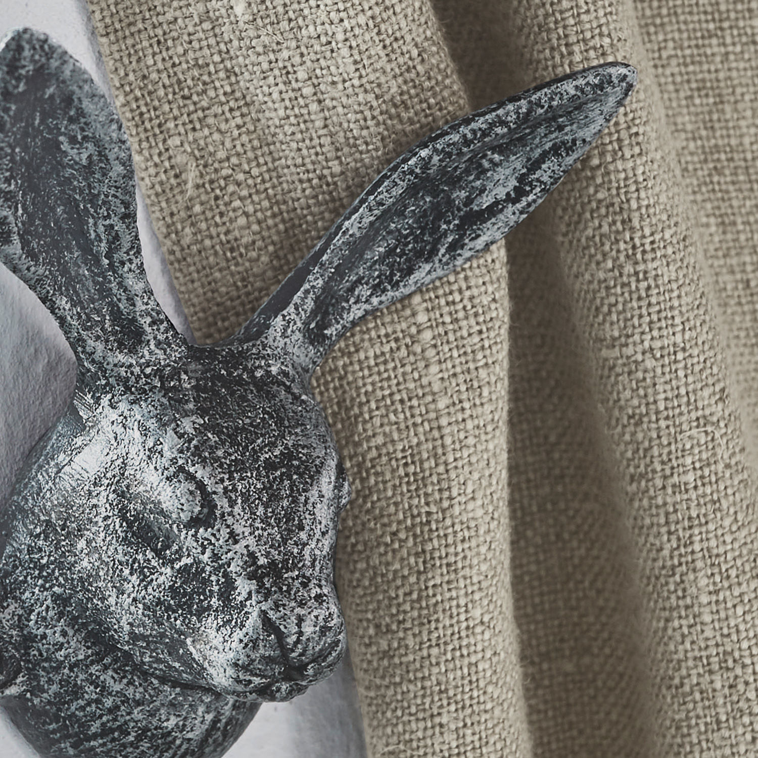 Dekorativer Hase aus grauem Metall vor beigem Strukturstoff als Wanddeko