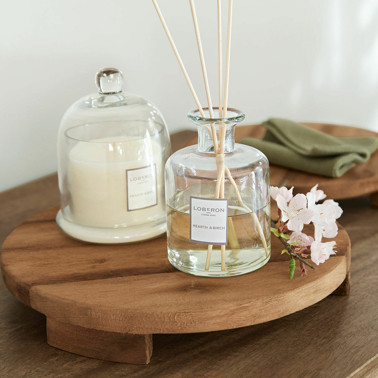 Glas-Duftspender und Kerze auf naturfarbenem Holztablett als Wohnaccessoire