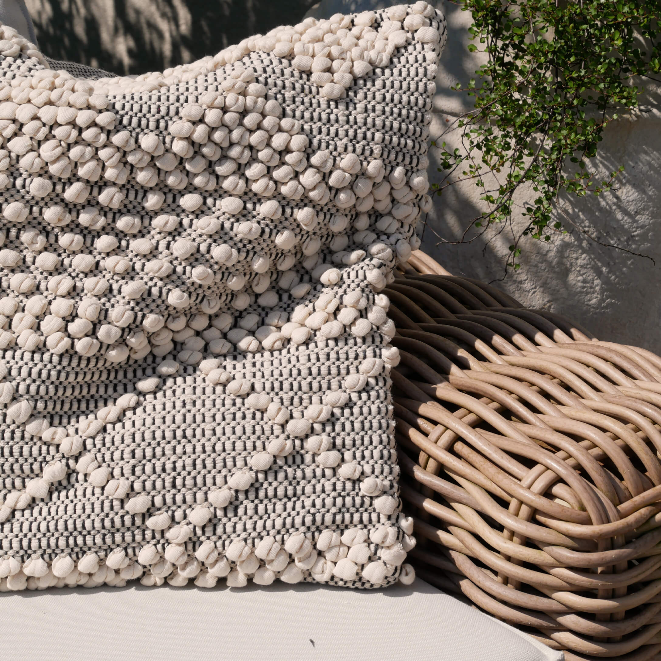 Dekoratives Baumwollkissen in Creme-Grau auf Rattansessel, stilvolle Wohnaccessoire