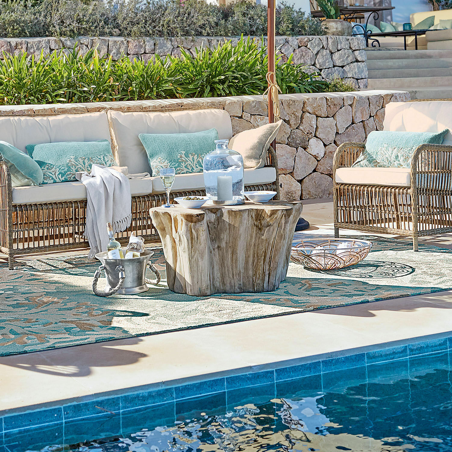 Gartenmöbel-Set aus Rattan mit cremefarbenen Kissen und Holztisch am Poolbereich