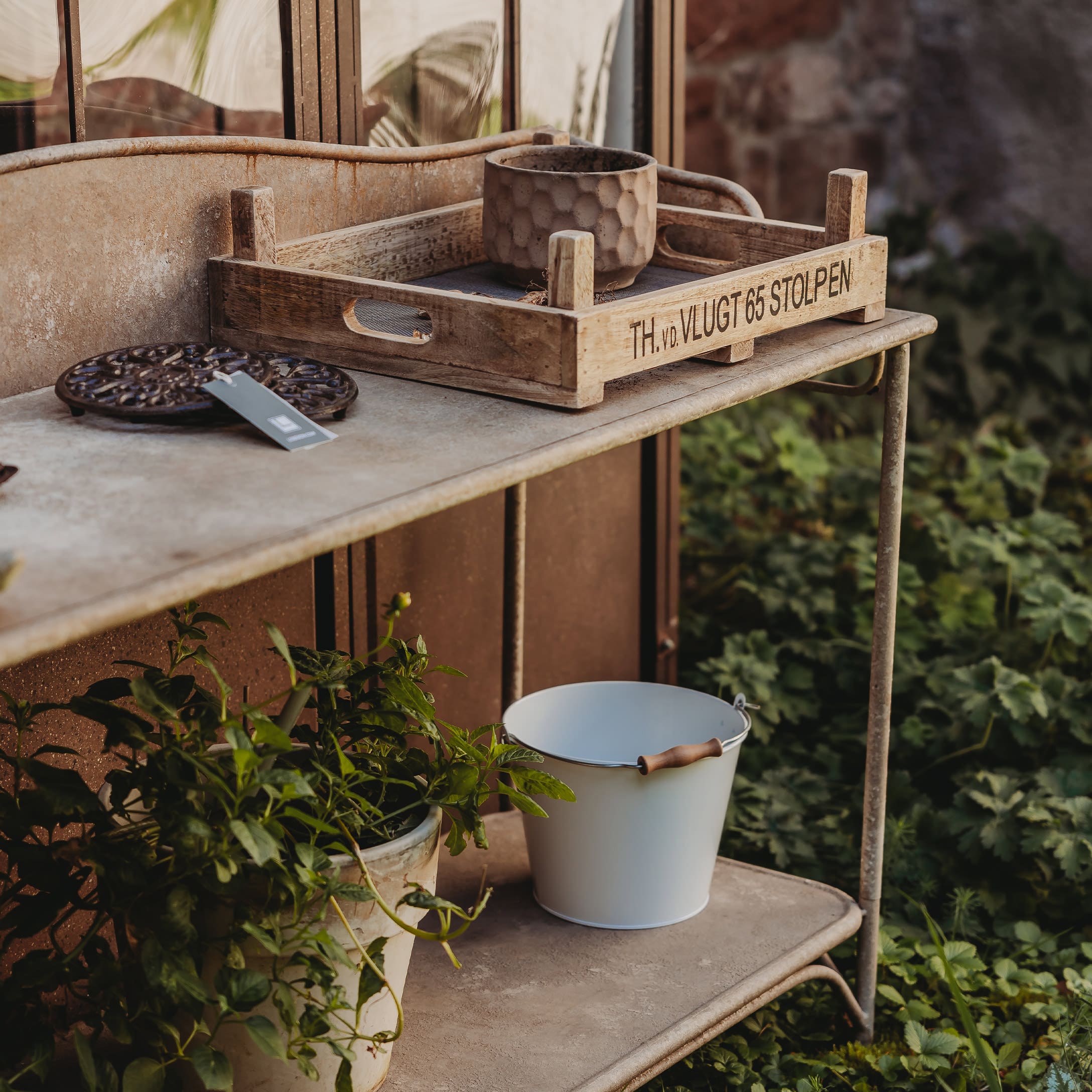 Holztablett auf Metalltisch mit Blumentopf und weißem Eimer im Garten als Dekoration