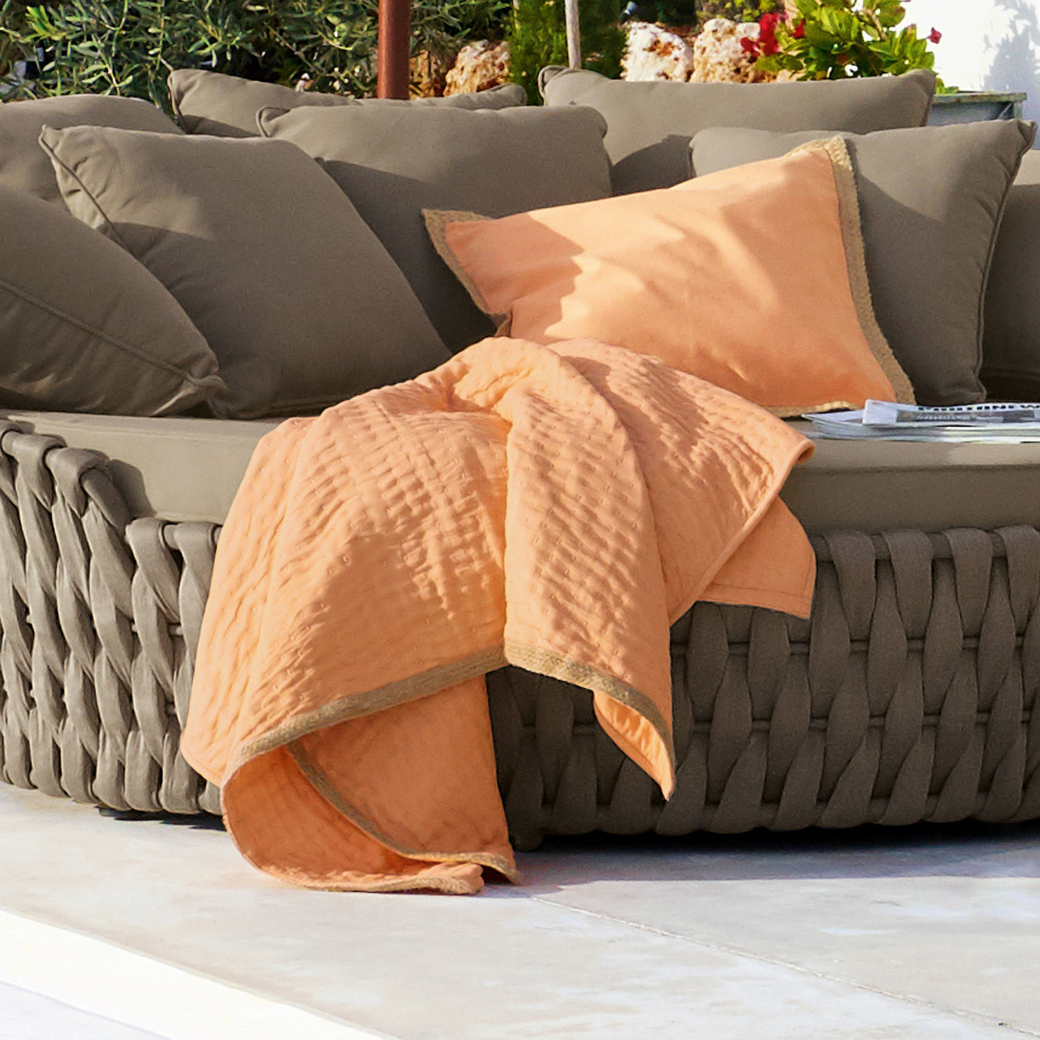 Orangefarbene Baumwolldecke und Kissen auf grauem geflochtenem Sofa, Outdoor-Terrassendeko