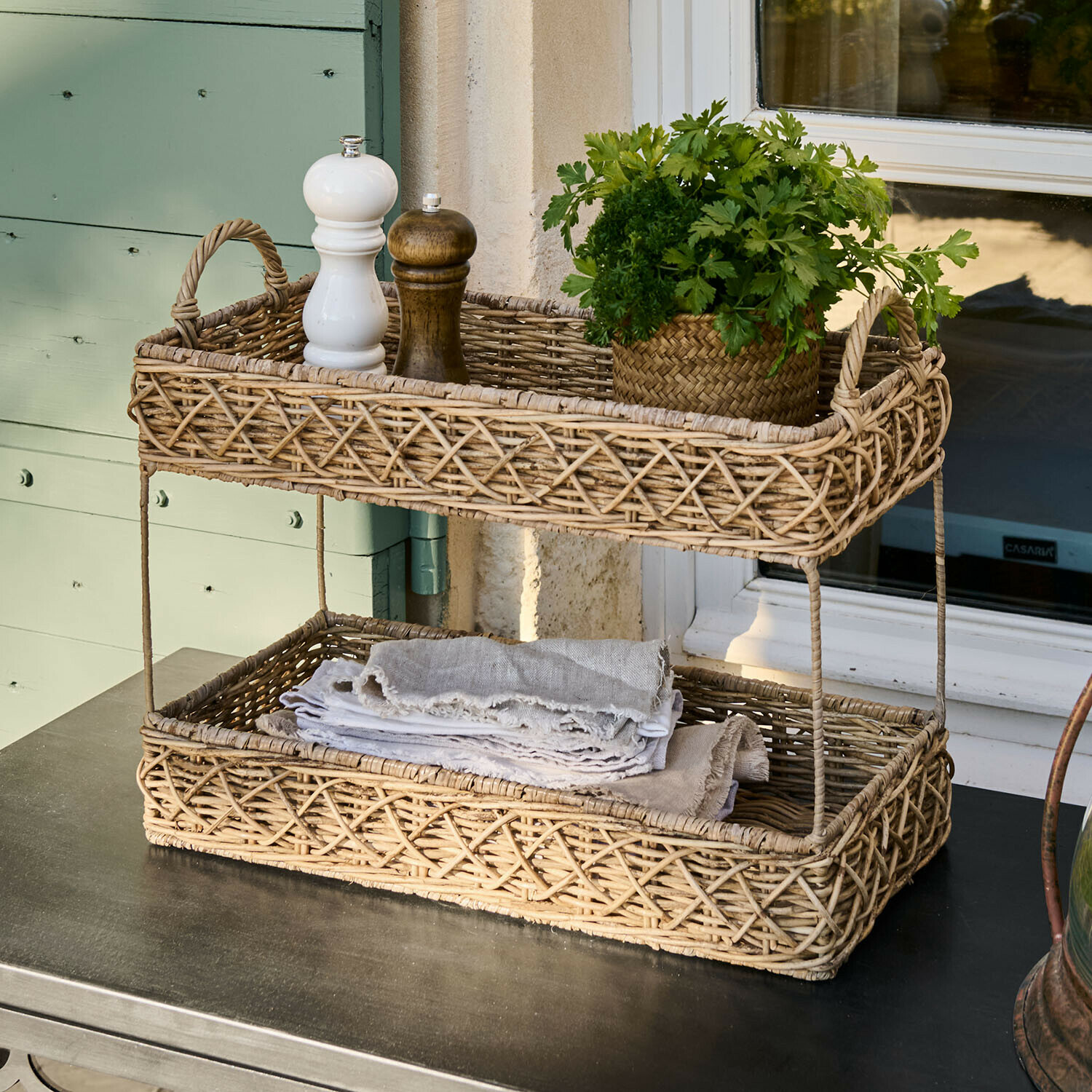 Zweistöckiger Korb aus natürlichem Rattan mit Gewürzen und frischen Kräutern auf Tisch